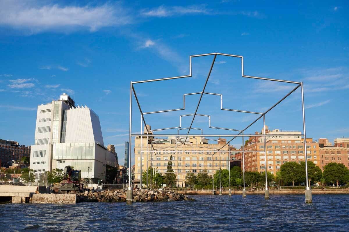 A color photograph of the Whitney Museum and neighboring buildings seen from the Hudson River. 