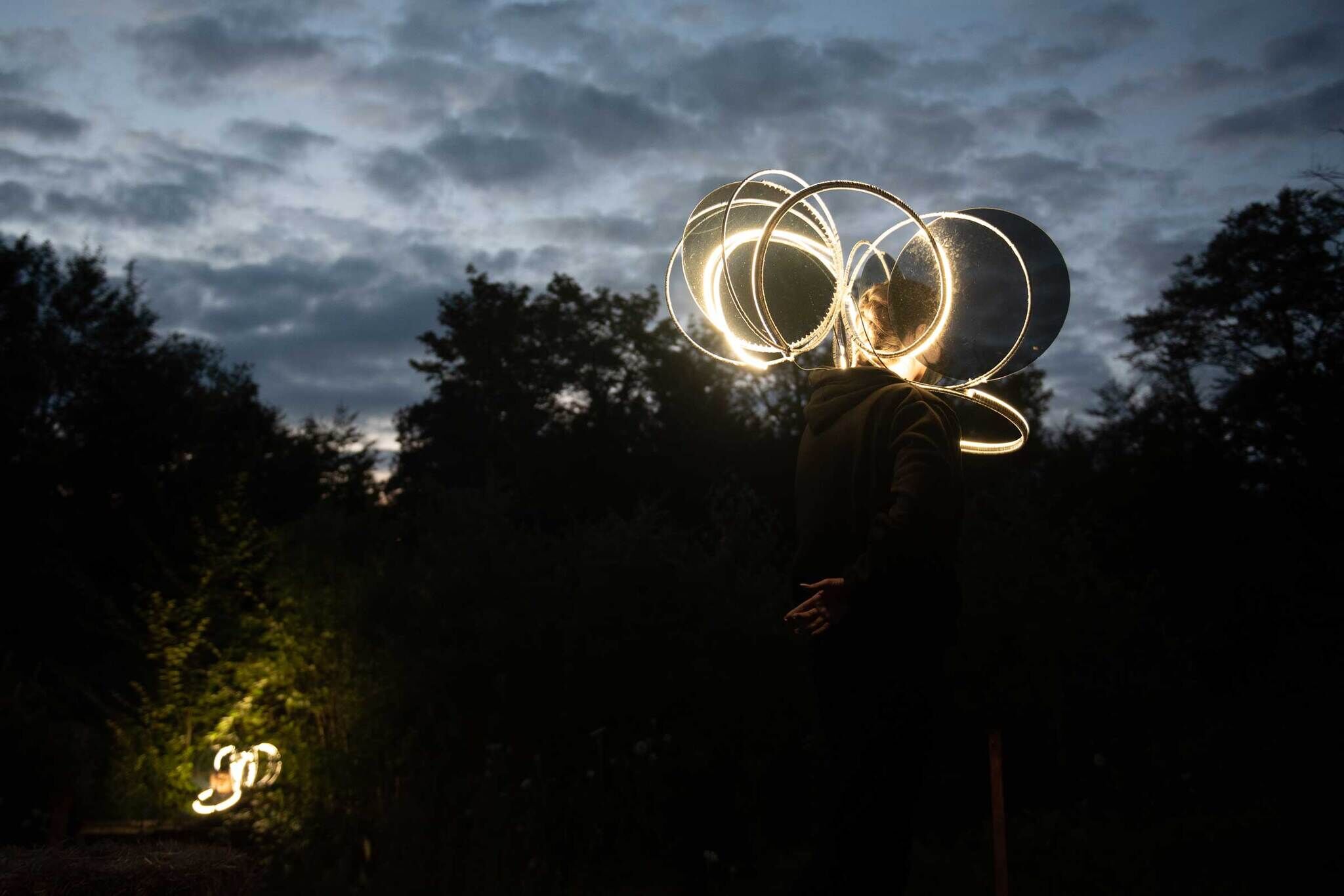 Person twirling illuminated hoops in the dark, with a cloudy sky and trees in the background.