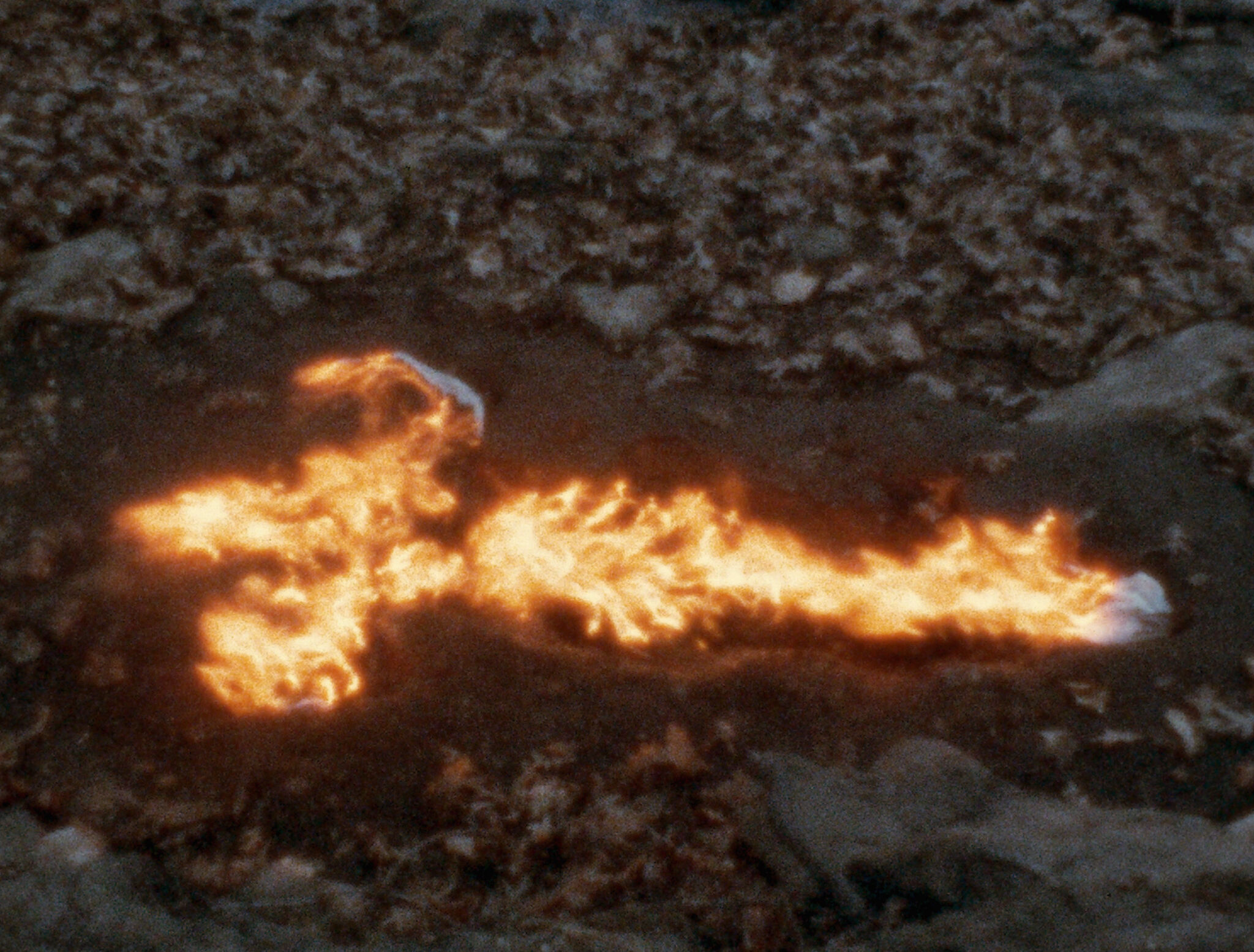 A figure-shaped fire burns on the ground surrounded by dark terrain.