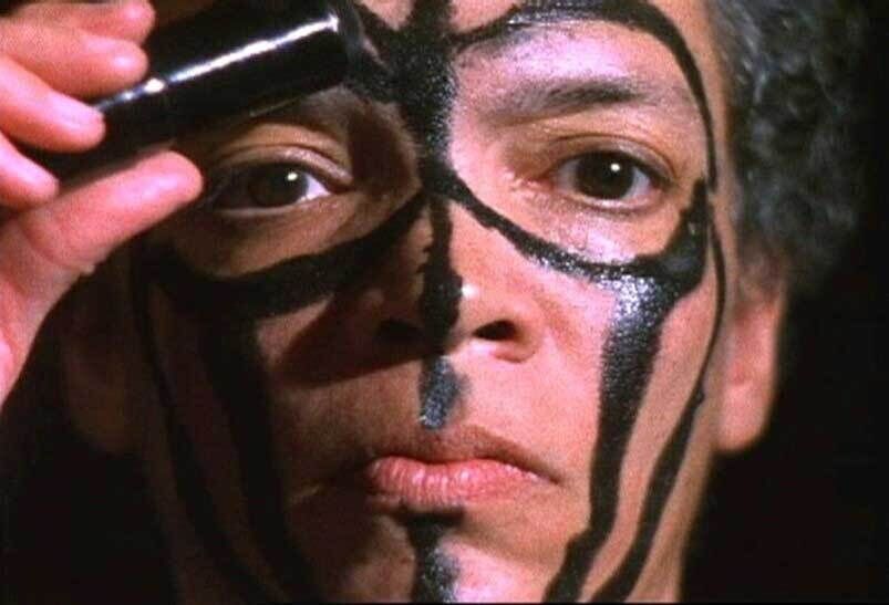 Person applying black face paint in intricate patterns, covering half of their face. The paint forms symmetrical lines and shapes.