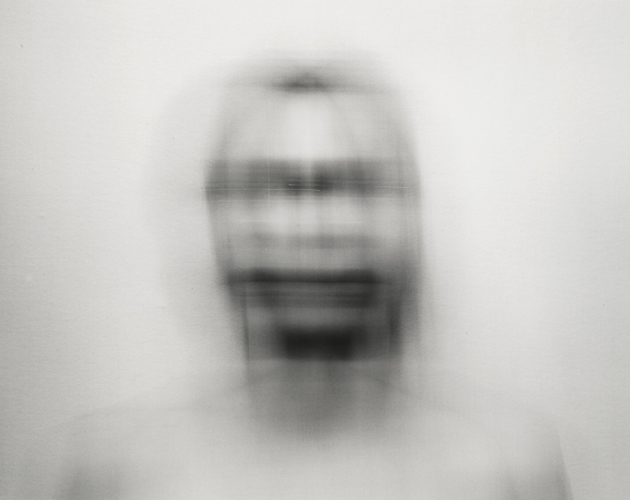 Blurry, abstract image of a human face with indistinct features, creating a distorted effect against a plain background.