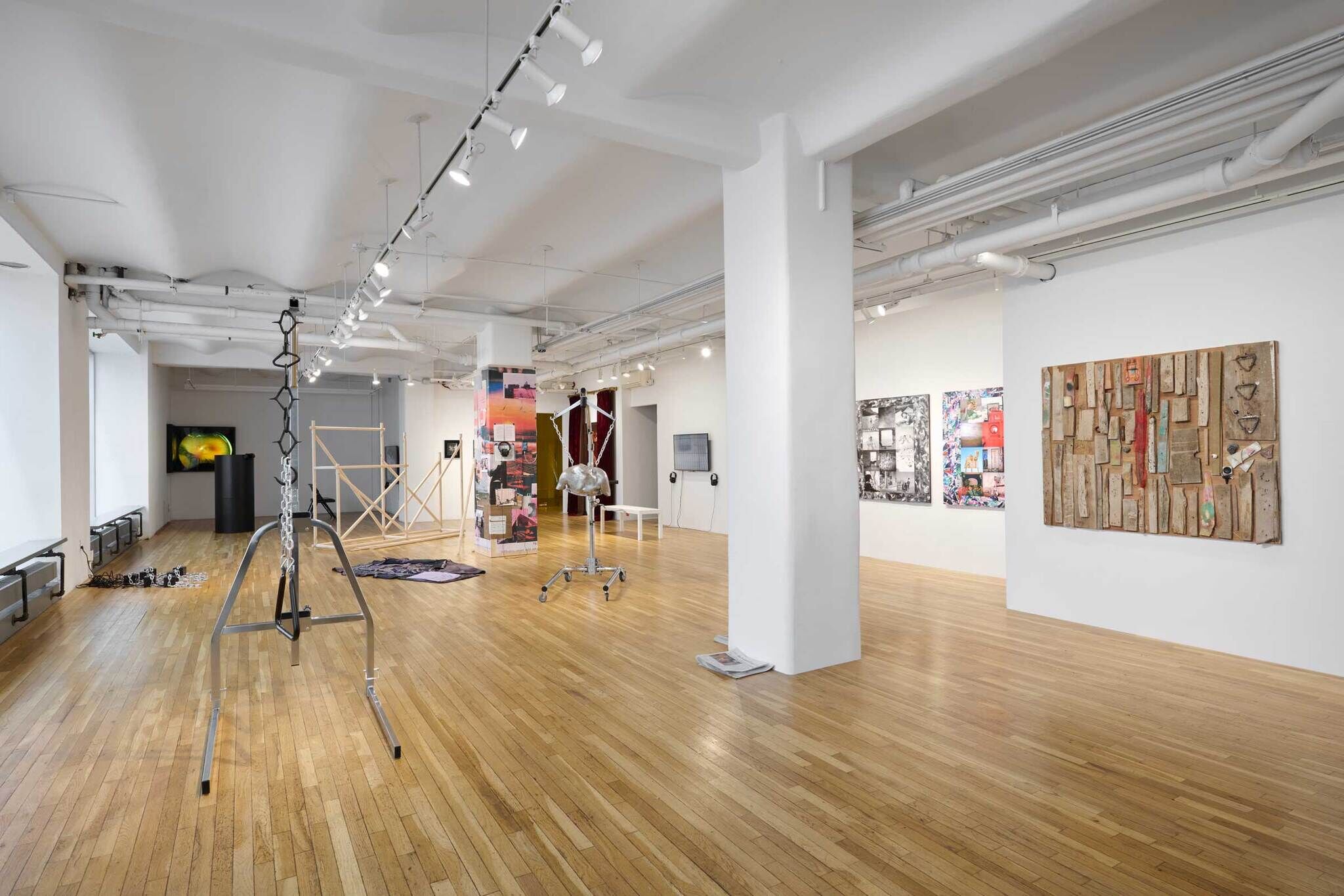 Modern art gallery with various installations, sculptures, and mixed media artworks displayed on white walls and wooden floors.