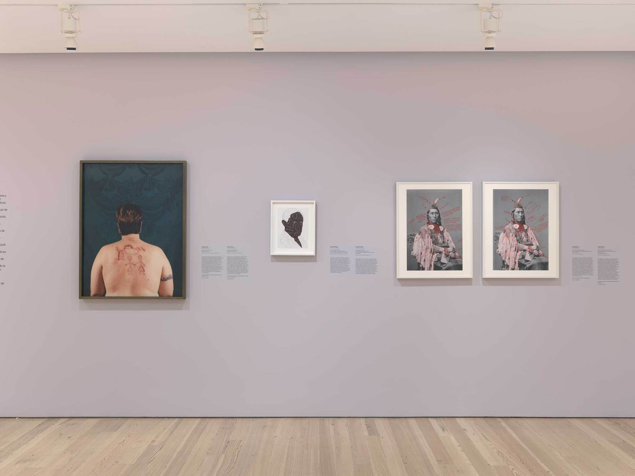 Art gallery wall displaying four framed artworks: a back view of a tattooed person, a silhouette portrait, and two identical images of a person in traditional attire.