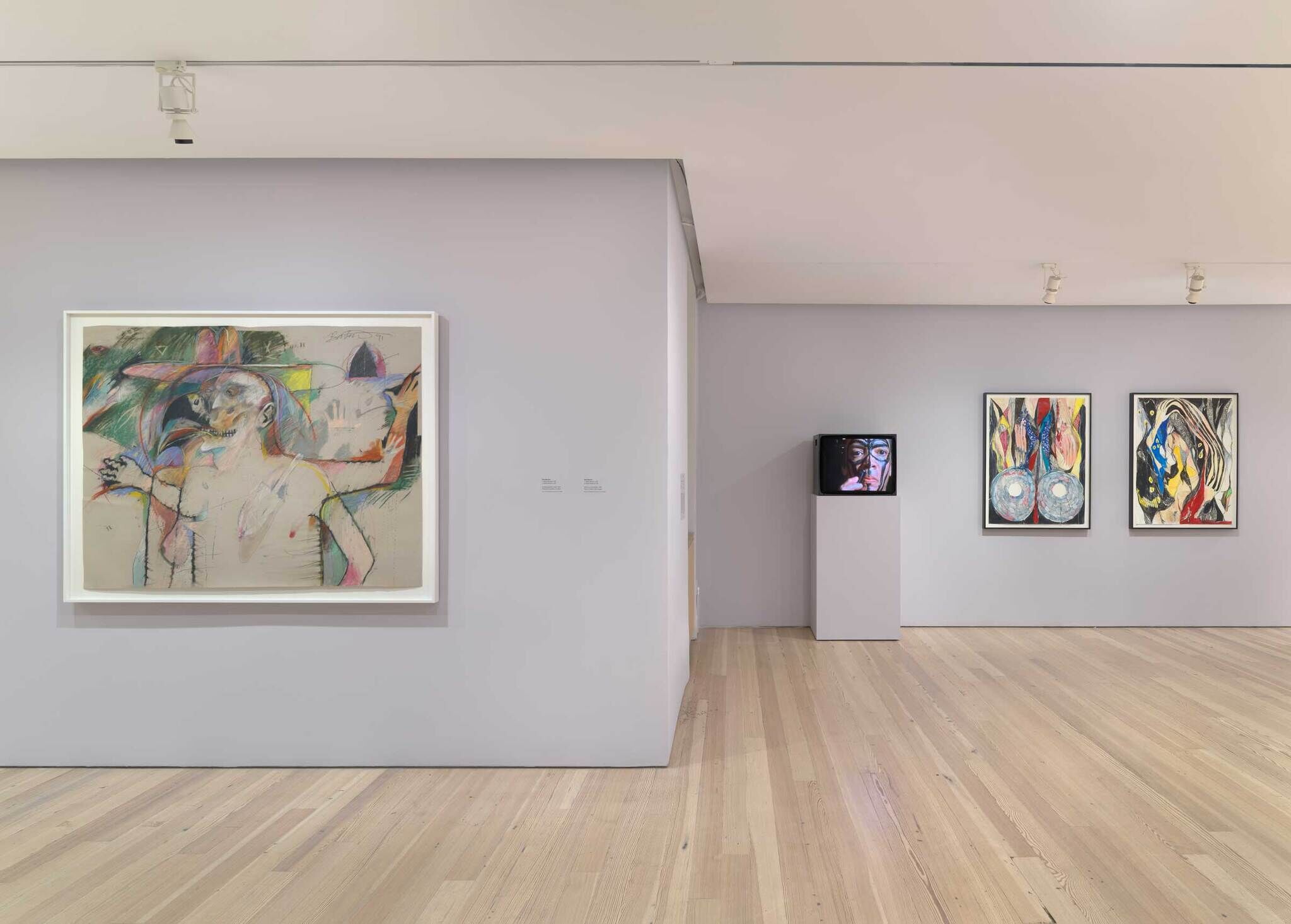 Art gallery with abstract paintings on walls and a TV displaying a face on a pedestal. Light wood flooring and white walls.