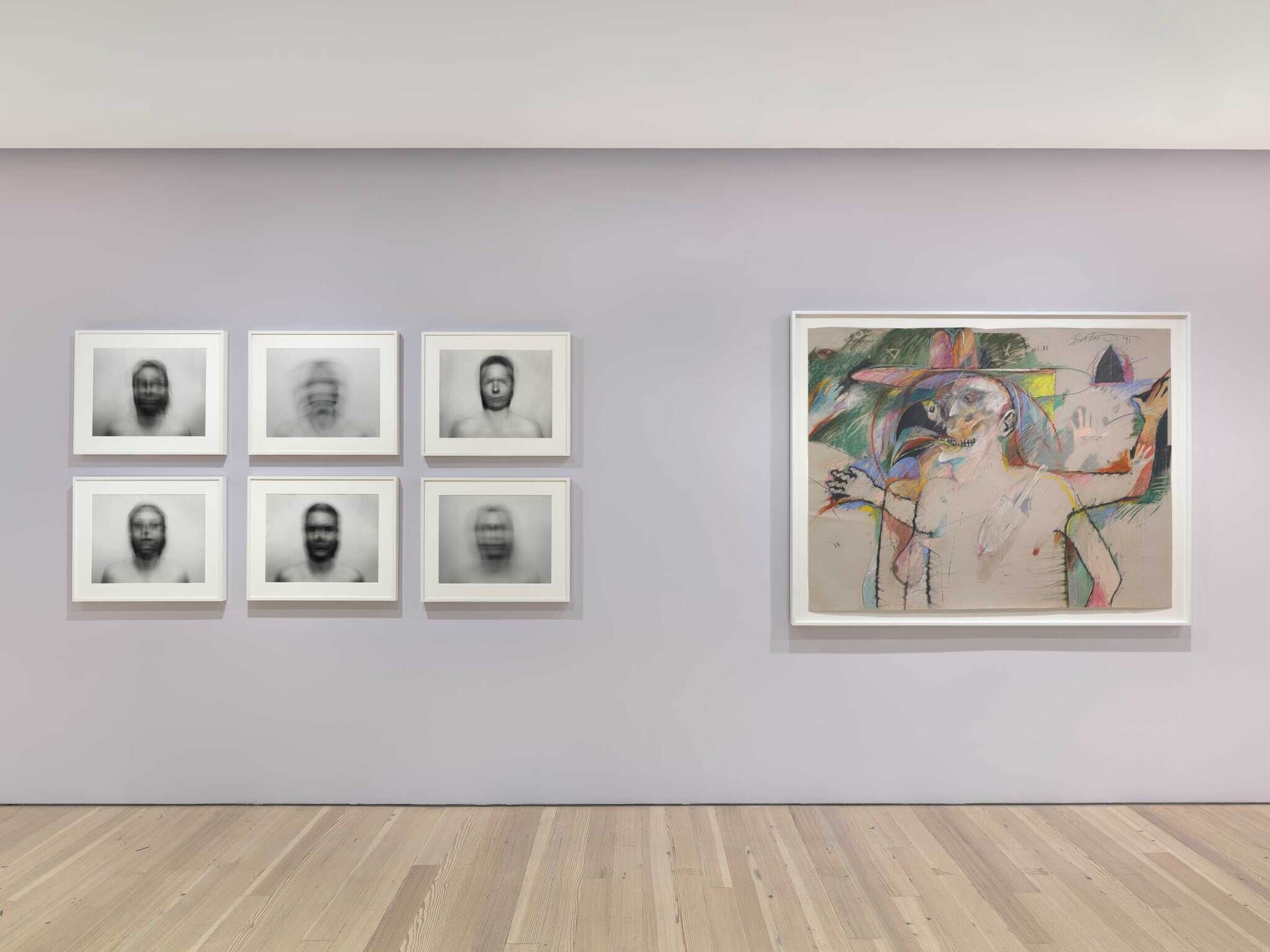 Art gallery wall with six blurred black-and-white portraits on the left and a colorful abstract painting of a figure on the right.