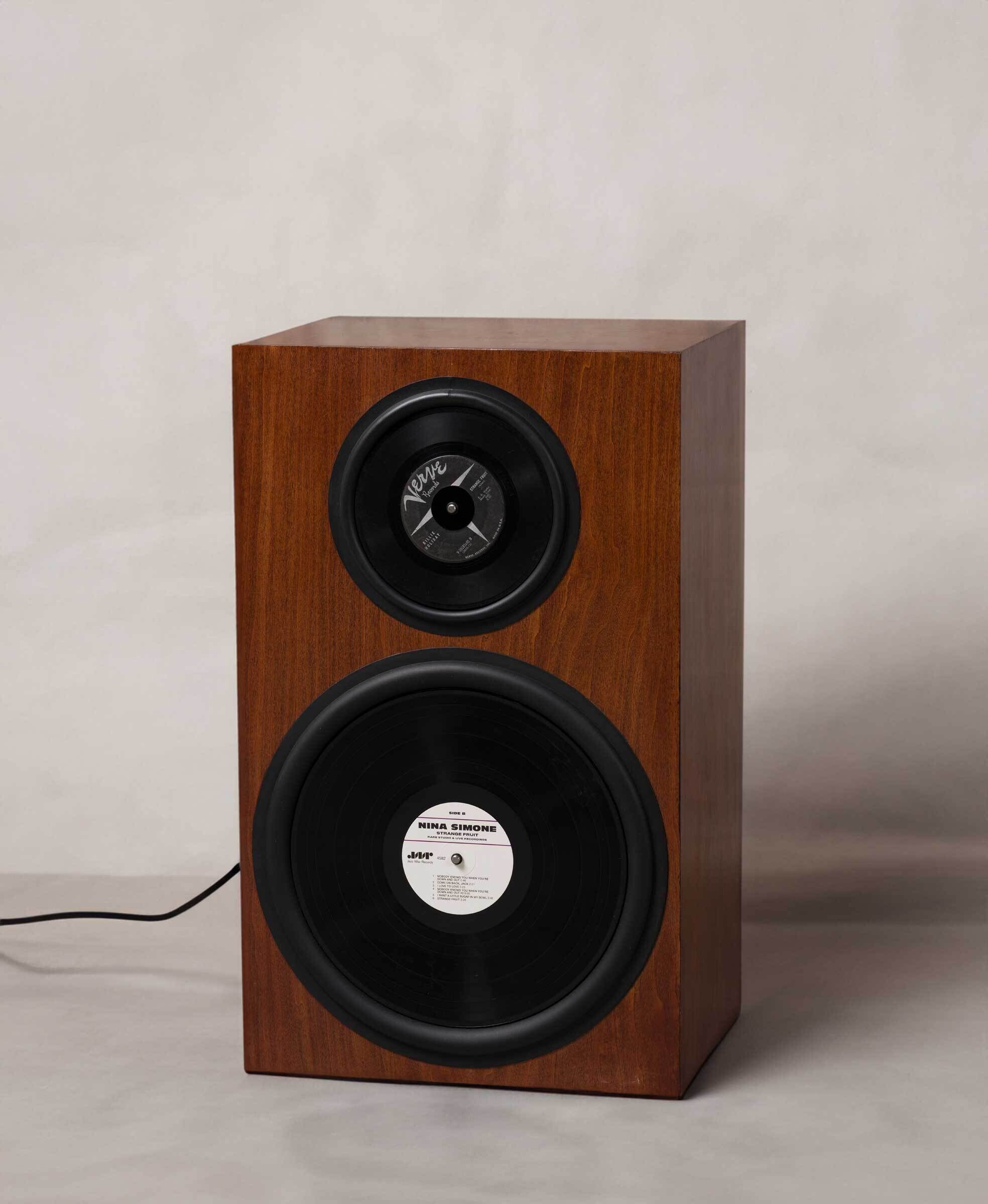 Wooden speaker with two vinyl records as drivers, one labeled "Nina Simone." The speaker is set against a plain background.