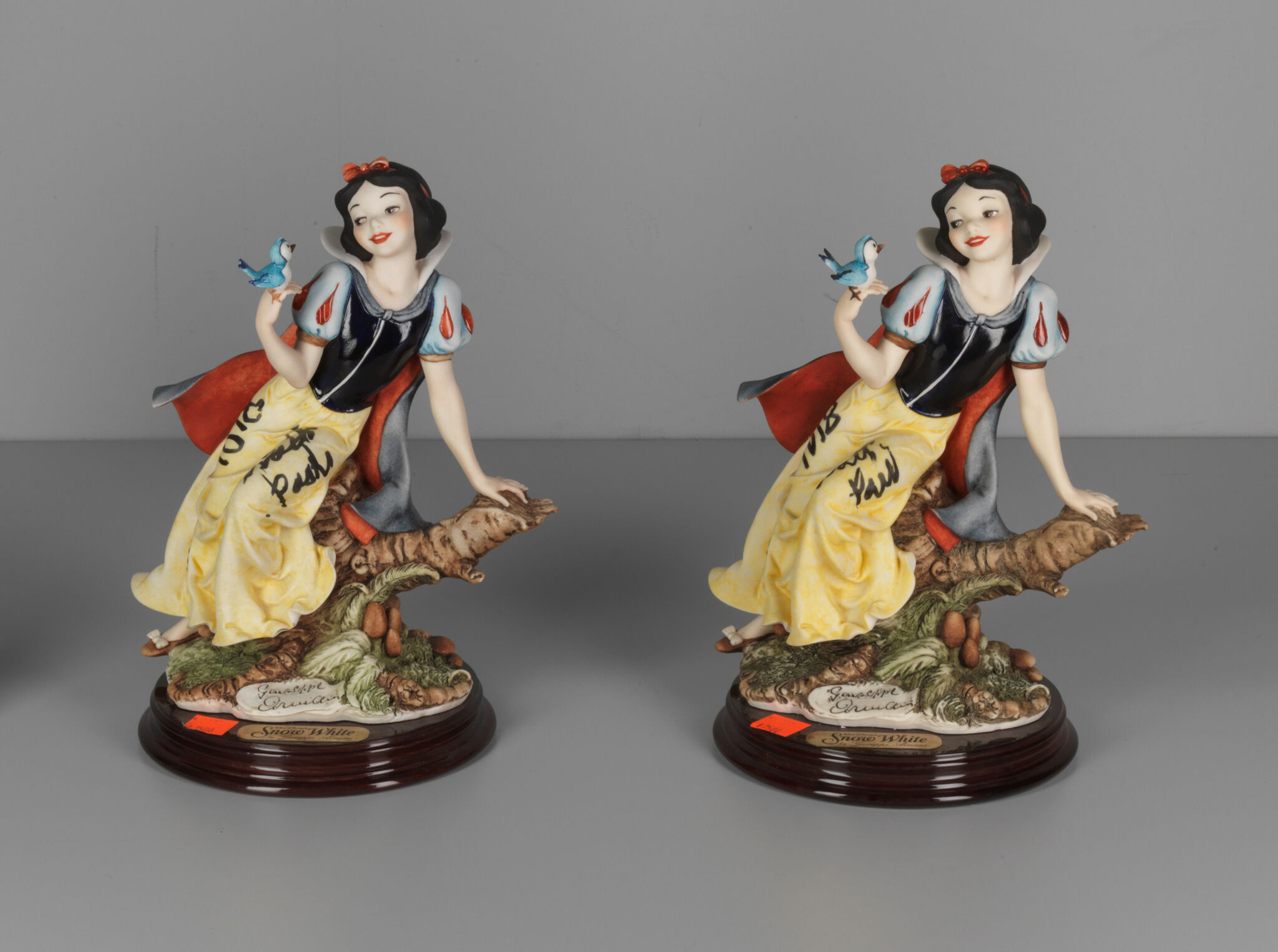 Two identical Snow White figurines, each holding a bluebird, sitting on a tree branch with a wooden base labeled "Snow White."