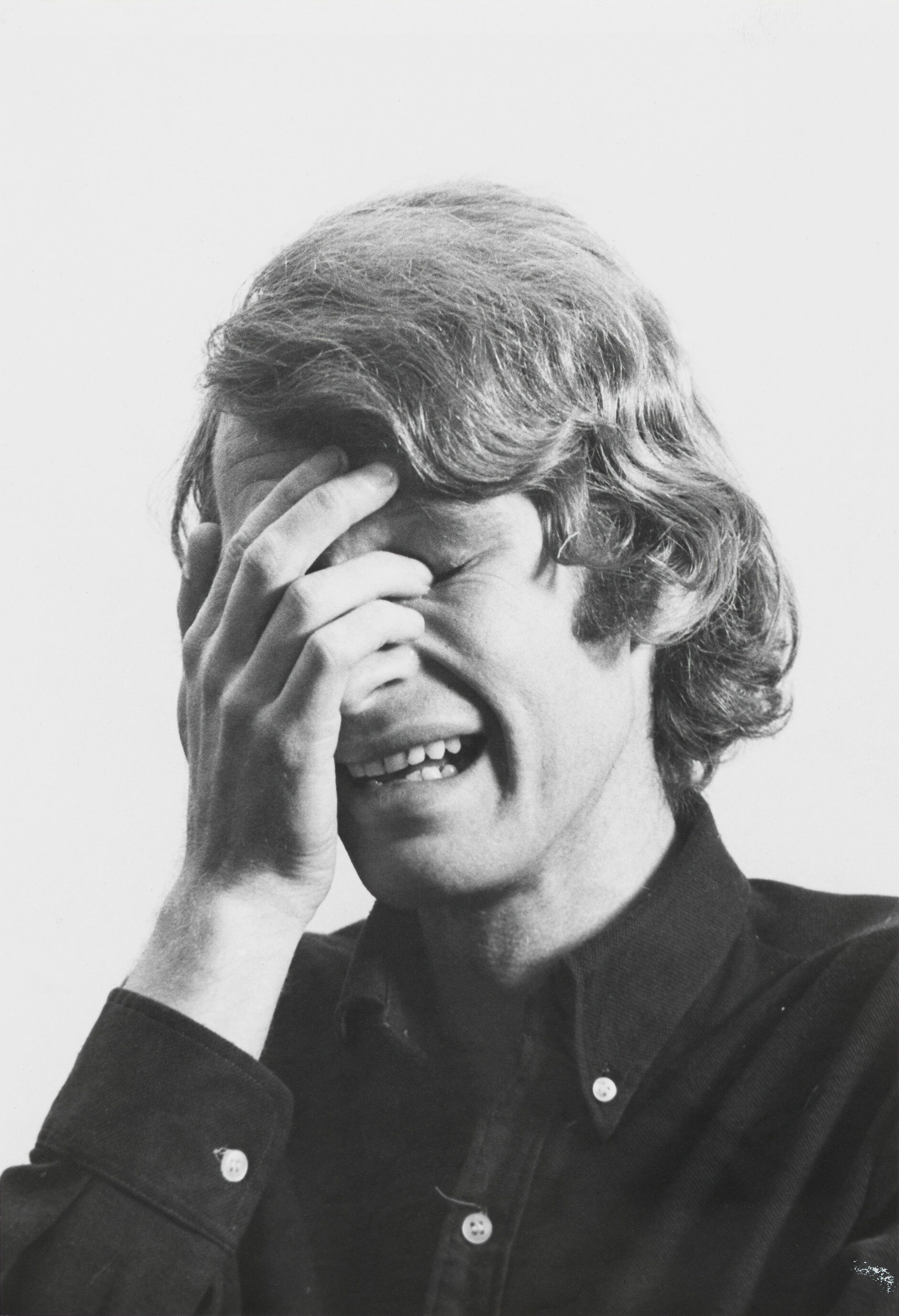 Black and white photo of a person with medium-length hair, covering their face with one hand, appearing to cry.