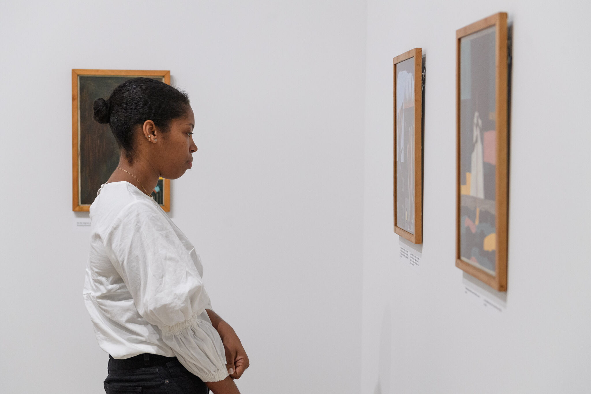 A woman in a white blouse observes framed artwork in a gallery.