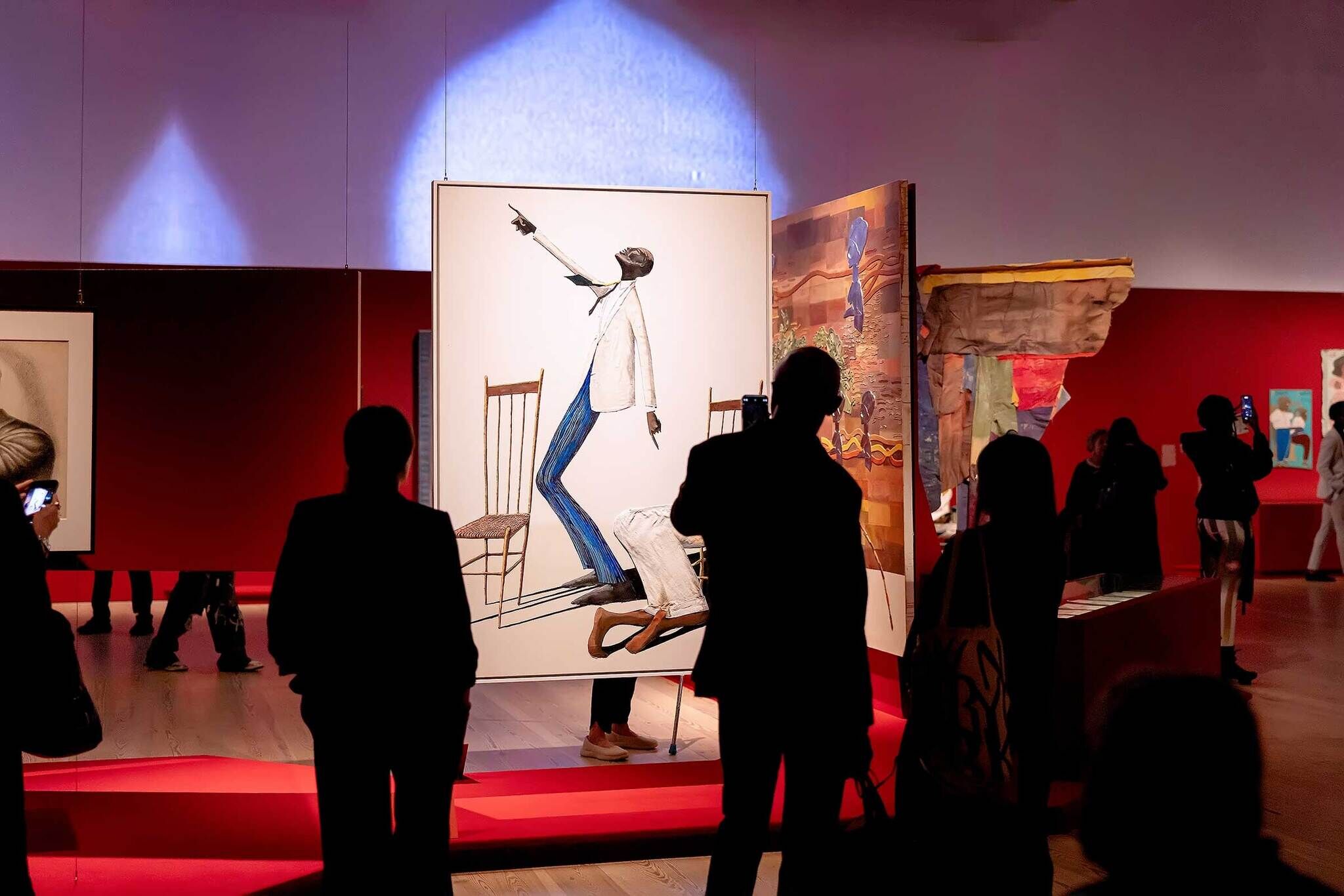 People viewing art in a gallery with red walls, featuring a prominent painting of a figure in a white jacket and blue pants.