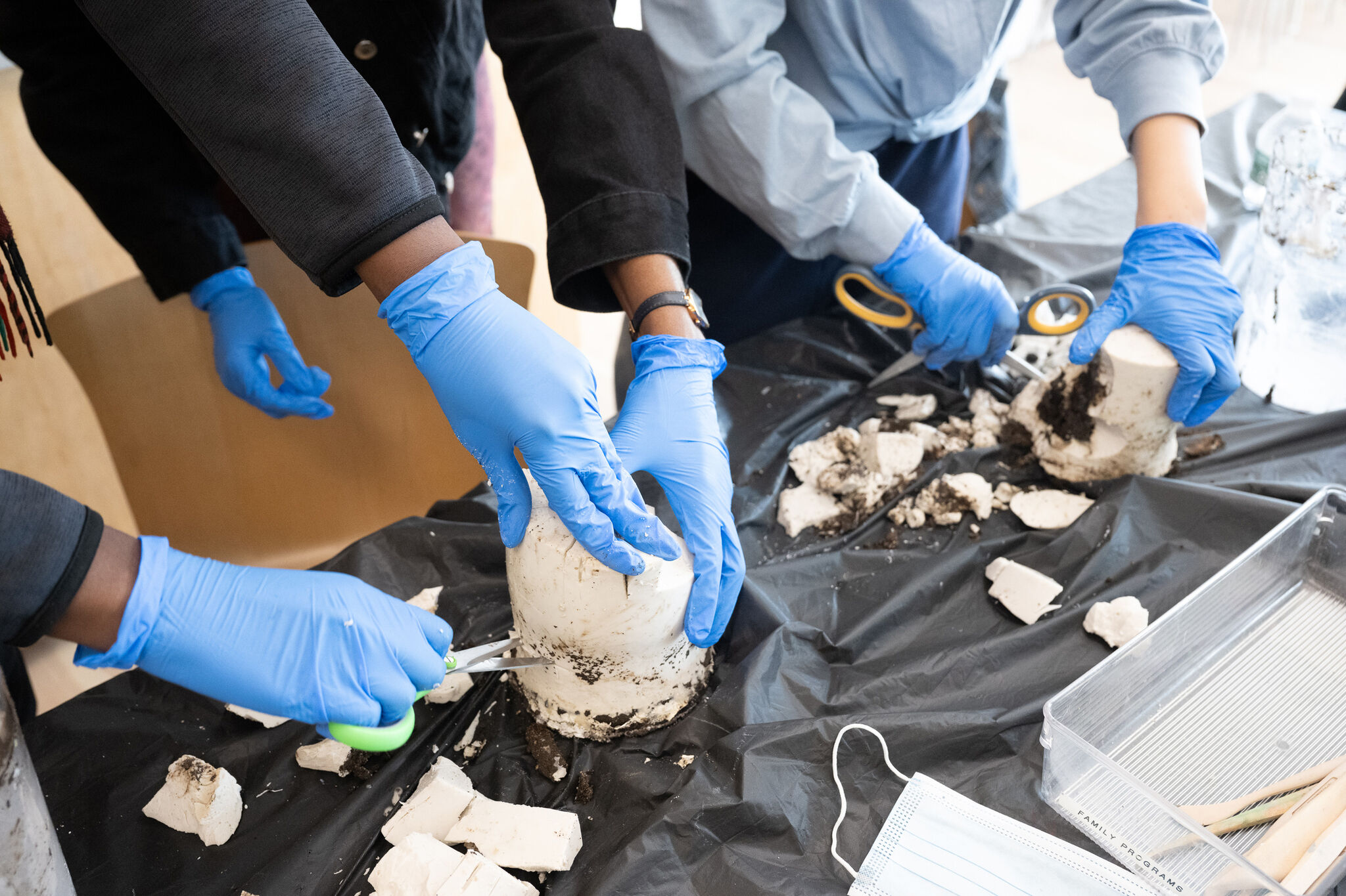 Students hold sculptures made of soil and plaster on a table.