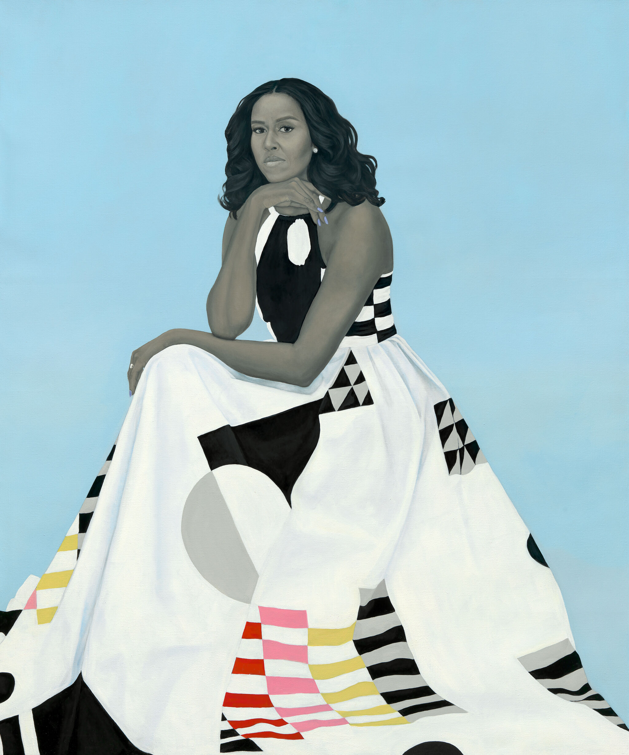 This image is a portrait of Michelle Obama seated, resting her chin on her hand. She is wearing a long, geometric-patterned dress that features bold black, white, red, pink and yellow shapes, including stripes, triangles, and circles. The dress covers much of the lower half of the image. The background is a soft, solid light blue and her hair is styled in loose waves. Her expression is calm yet contemplative. 