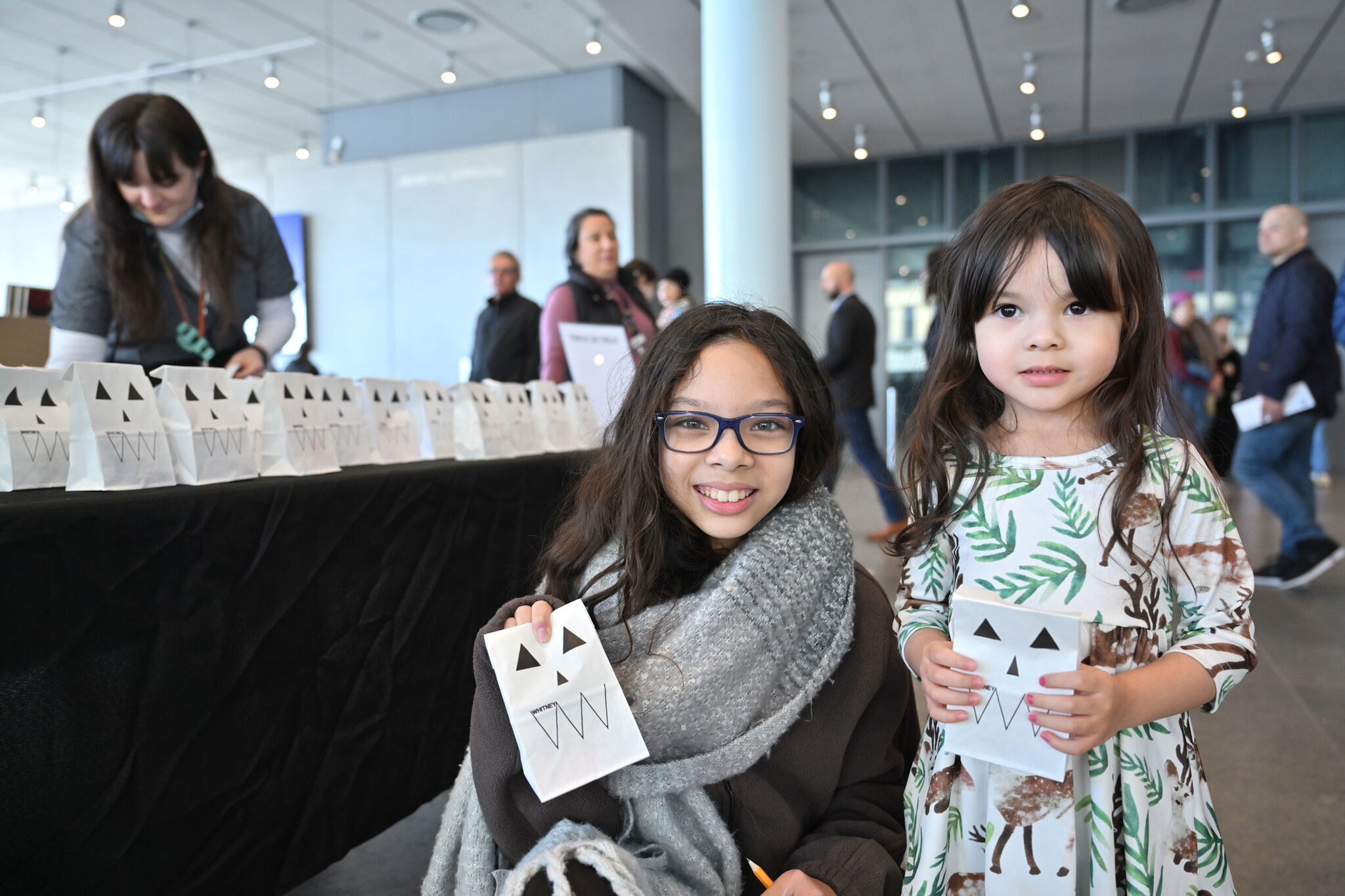 Two children smile while holding paper bags with jack-o'-lantern faces. 