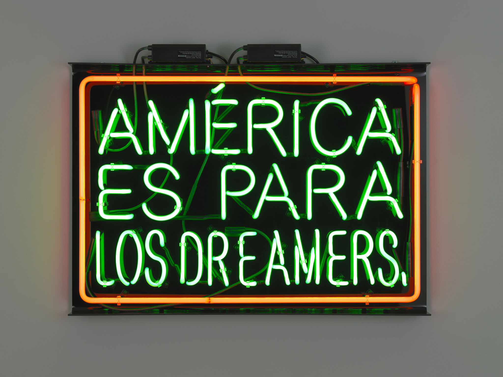 Neon sign with green and orange lights reads "AMÉRICA ES PARA LOS DREAMERS" on a dark background.