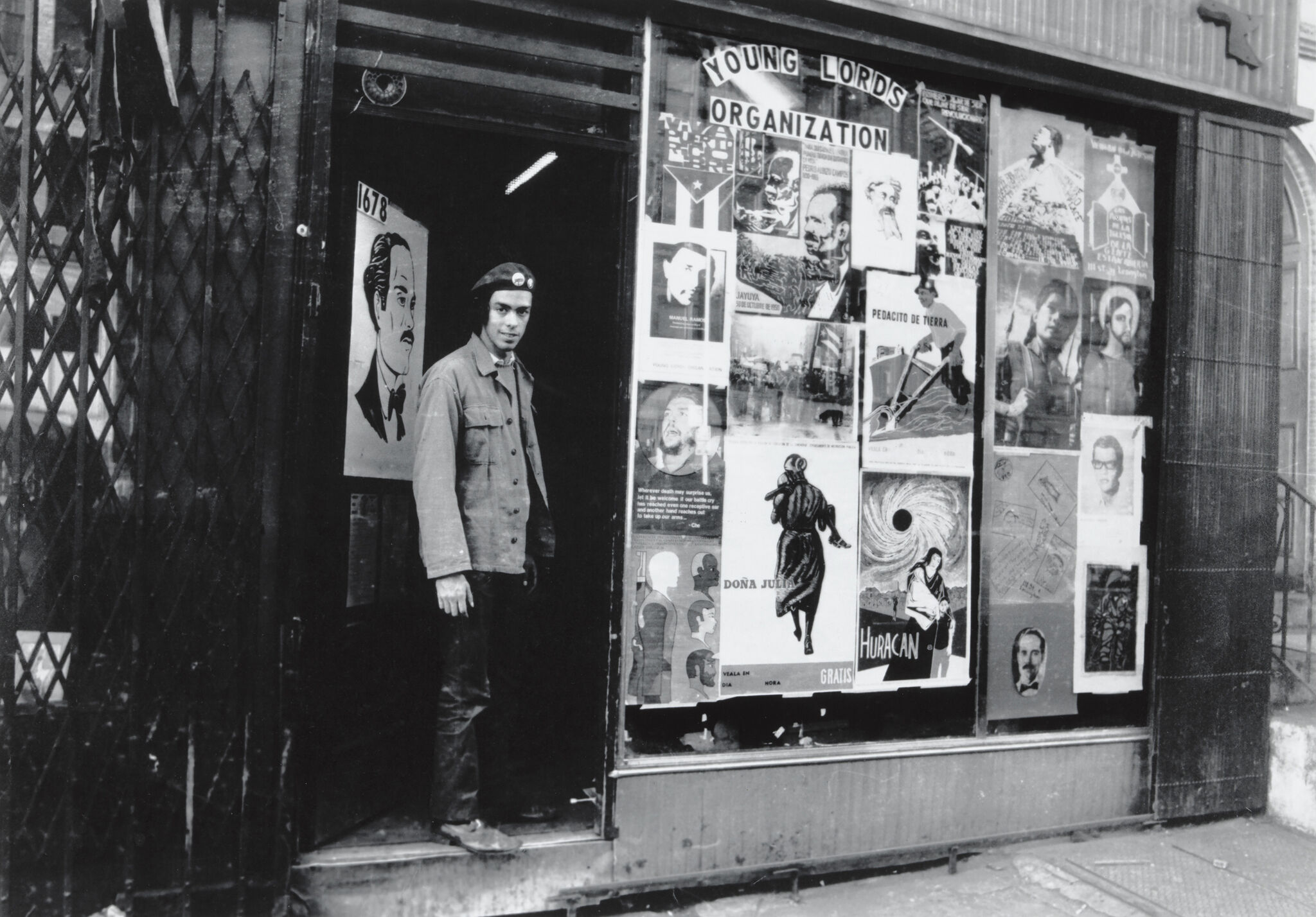 Person in a beret stands in the doorway of a building with "Young Lords Organization" posters covering the windows.