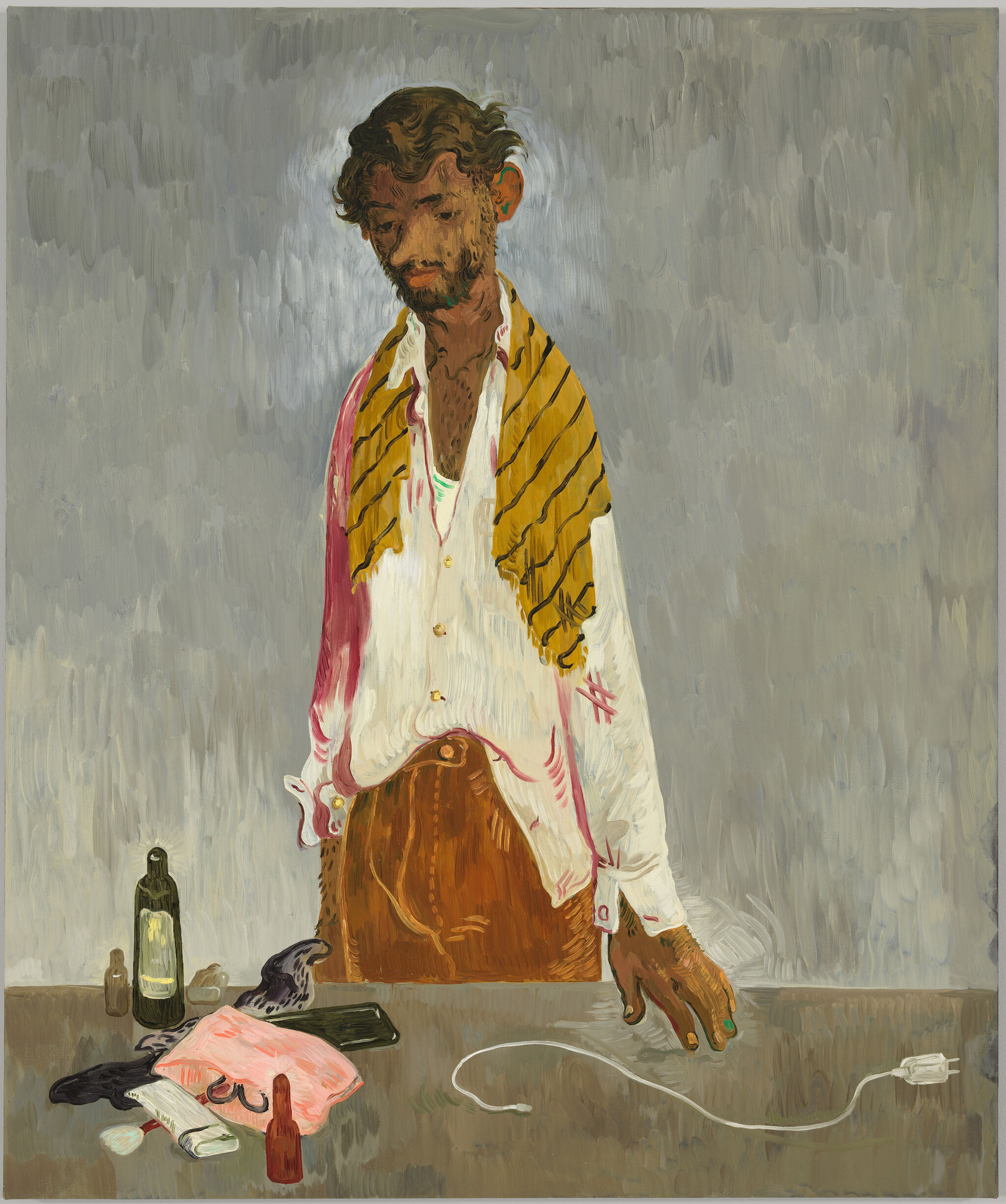 A man with a yellow-striped scarf stands at a table with bottles, a phone, and a charger, wearing a white shirt and brown pants.