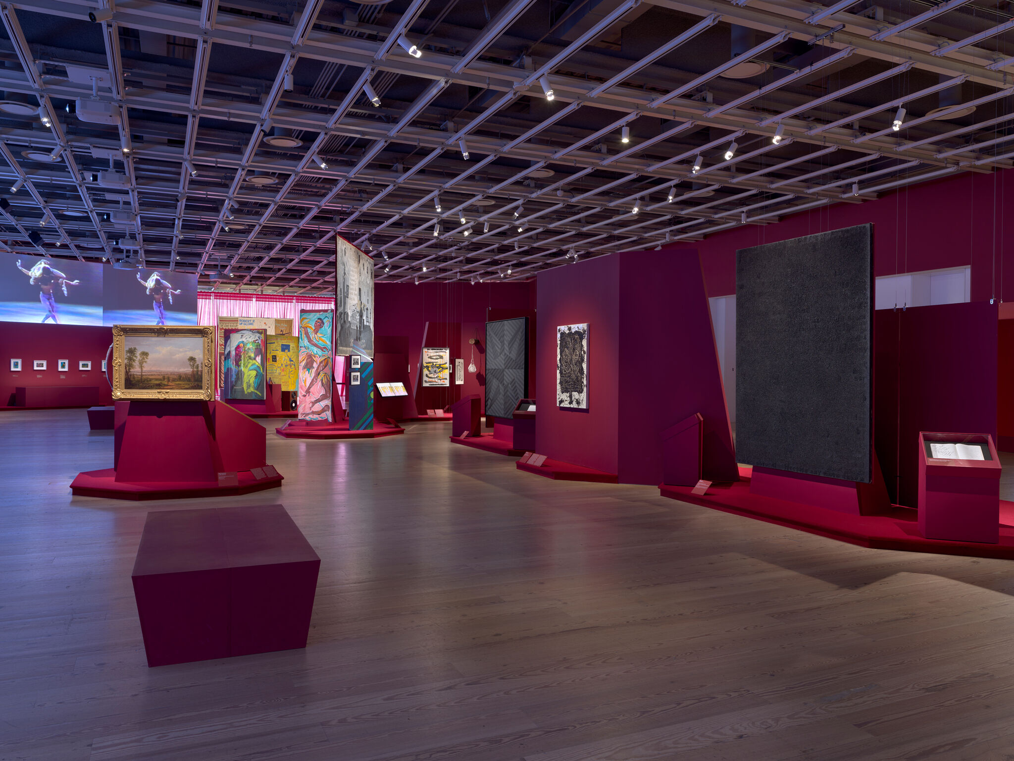 Art gallery with vibrant red walls, featuring various paintings and digital displays. 