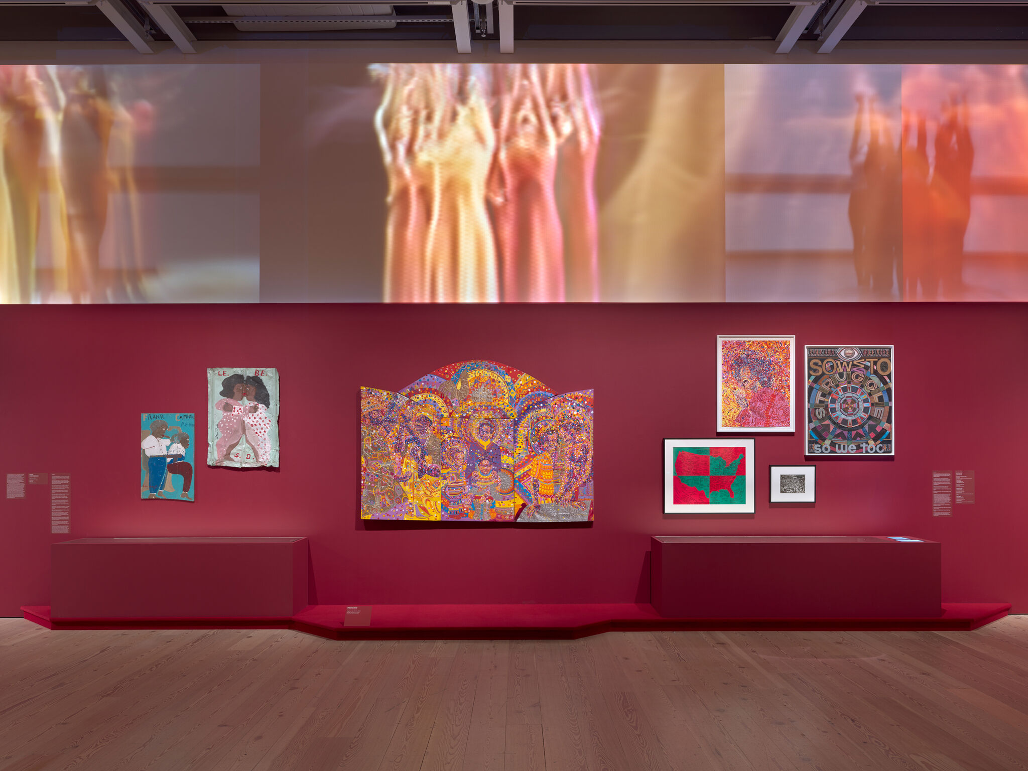 Art gallery wall with vibrant paintings and mixed media on a deep red background, featuring abstract and figurative designs.