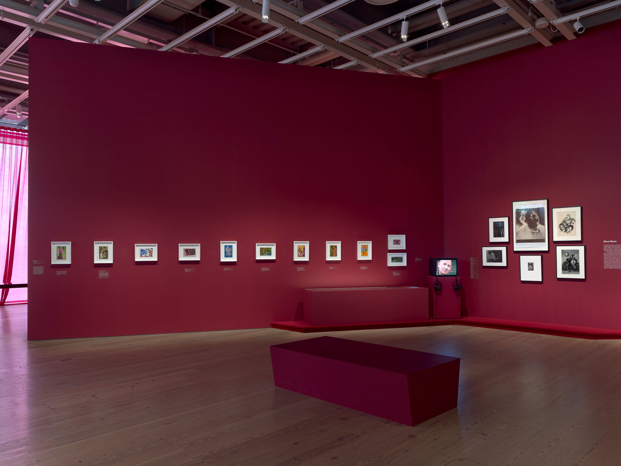 Art gallery with red walls displaying framed artworks and photographs. 