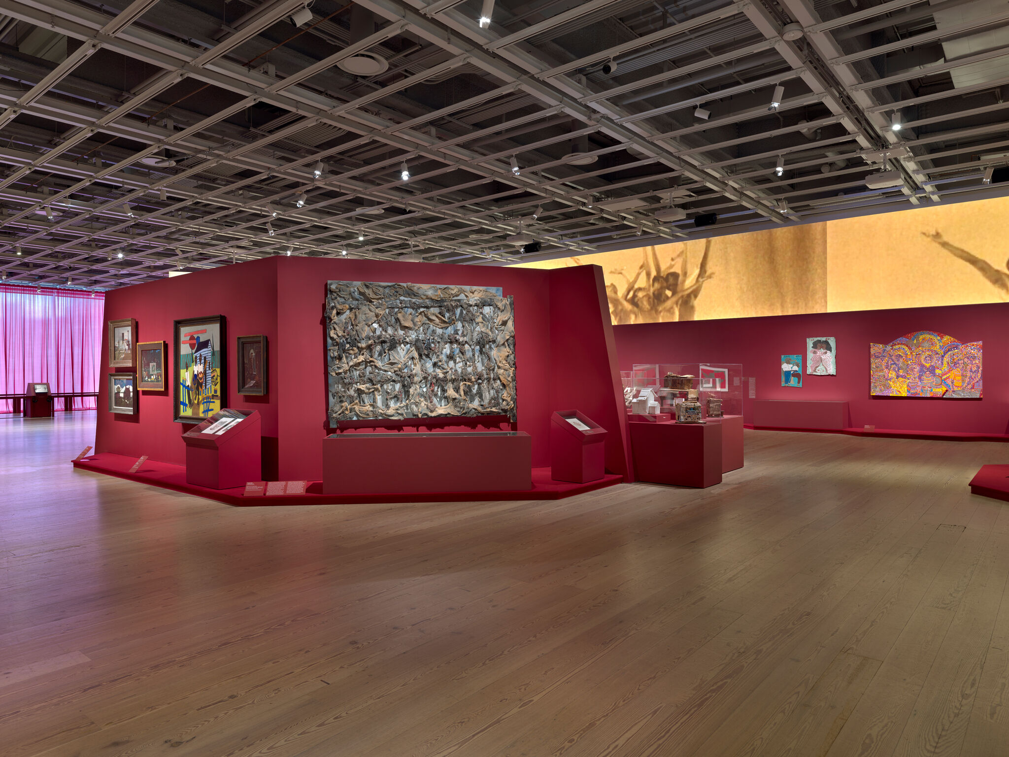 Art gallery with red walls displaying various paintings and sculptures. 