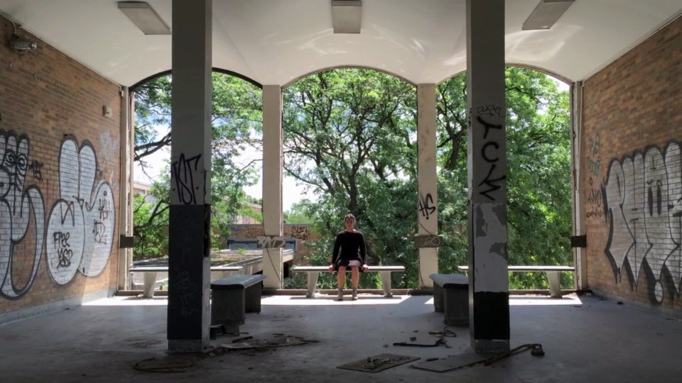 Person sitting on a bench in a graffiti-covered, open-air structure with trees visible in the background.