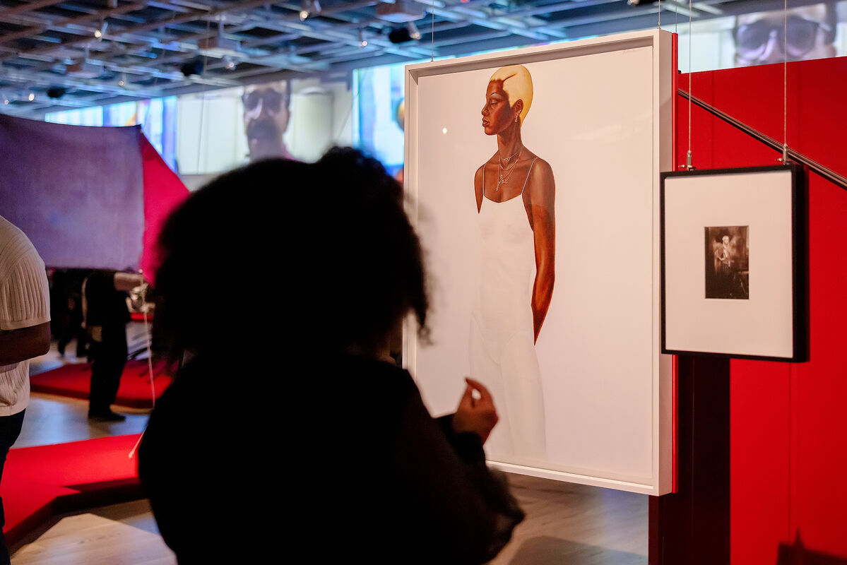 A woman is observing two artworks in front of her: "Dancer" Barkley Hendricks (1977) and "Dancer" by James Van Der Zee (1925). A wrap-around video projection can be seen in the background. 