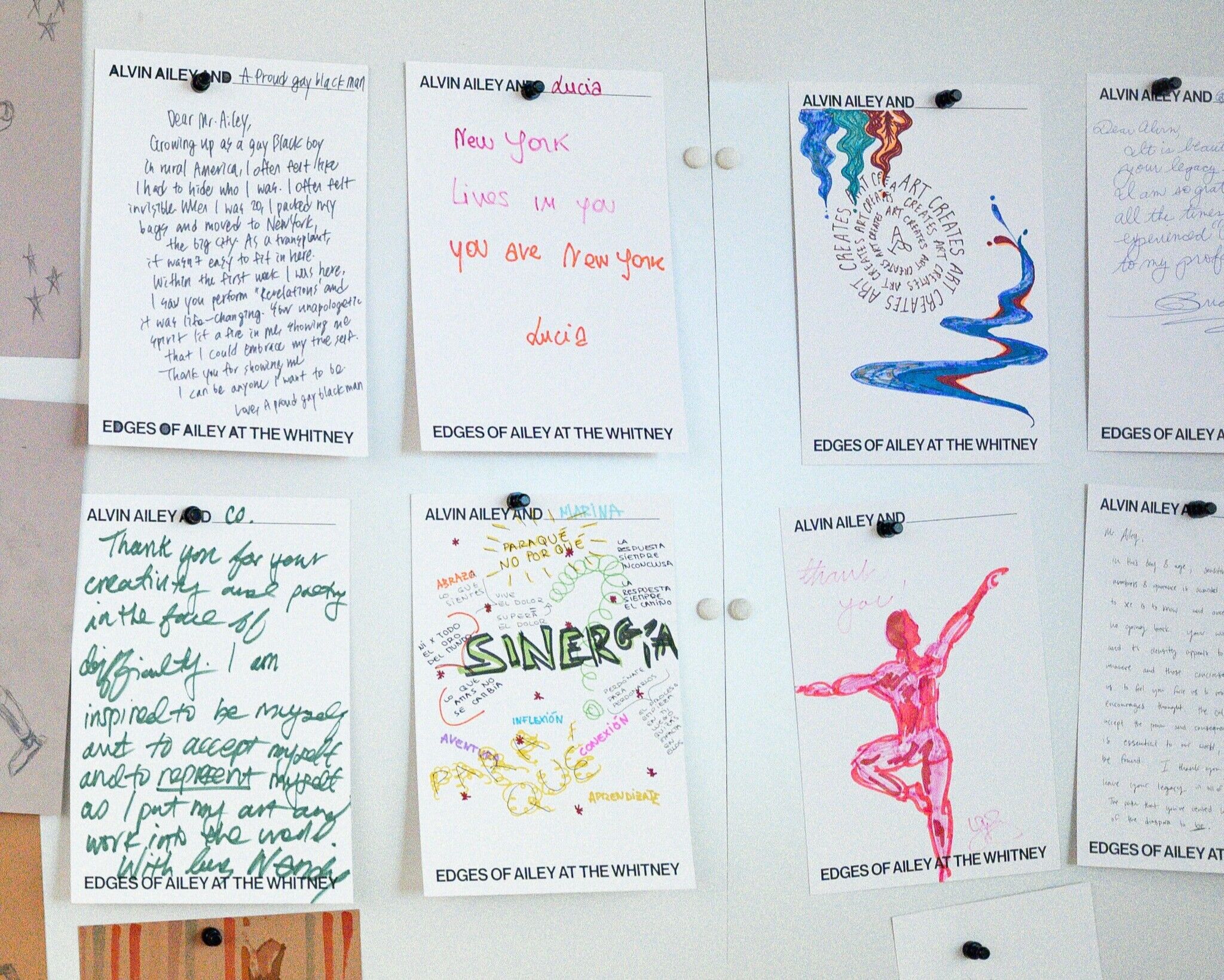 A selection of letters written to Alvin Ailey, containing colorful writing and drawings, are pinned on a white magnetic board. 