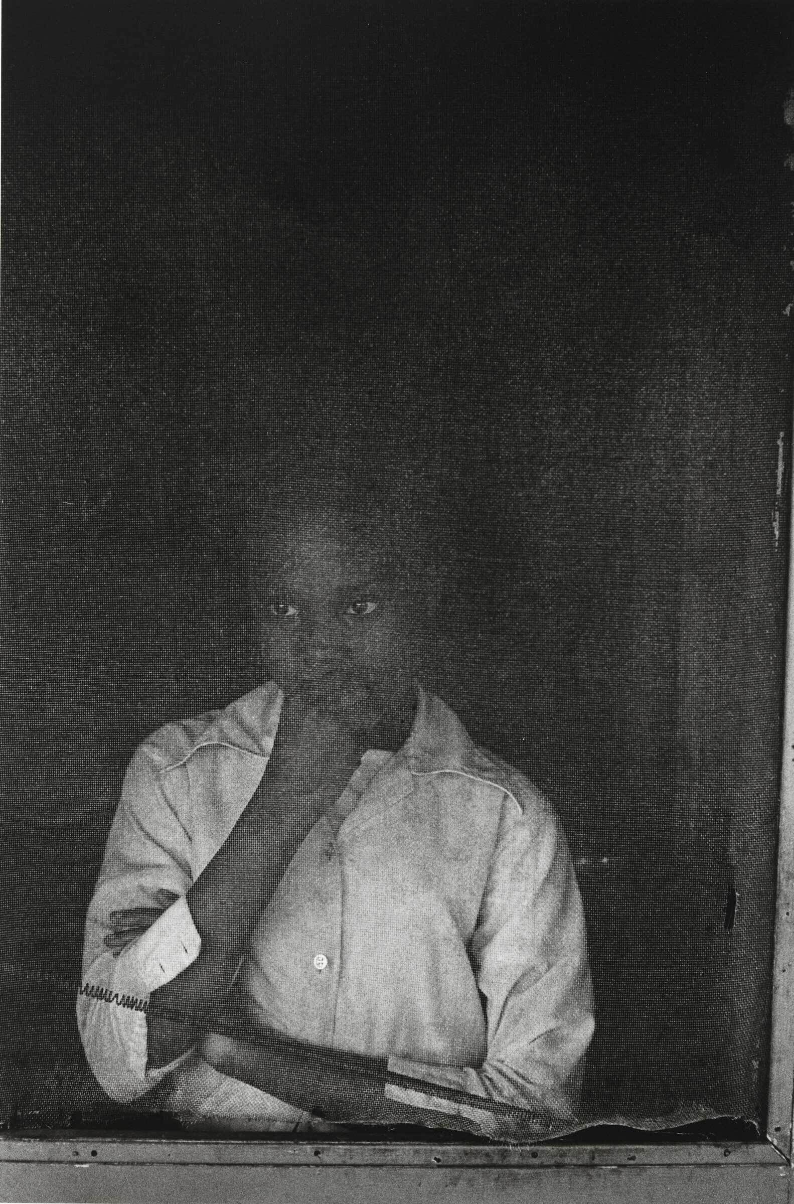 A person in a white shirt stands behind a screen, looking contemplative with a hand on their chin.