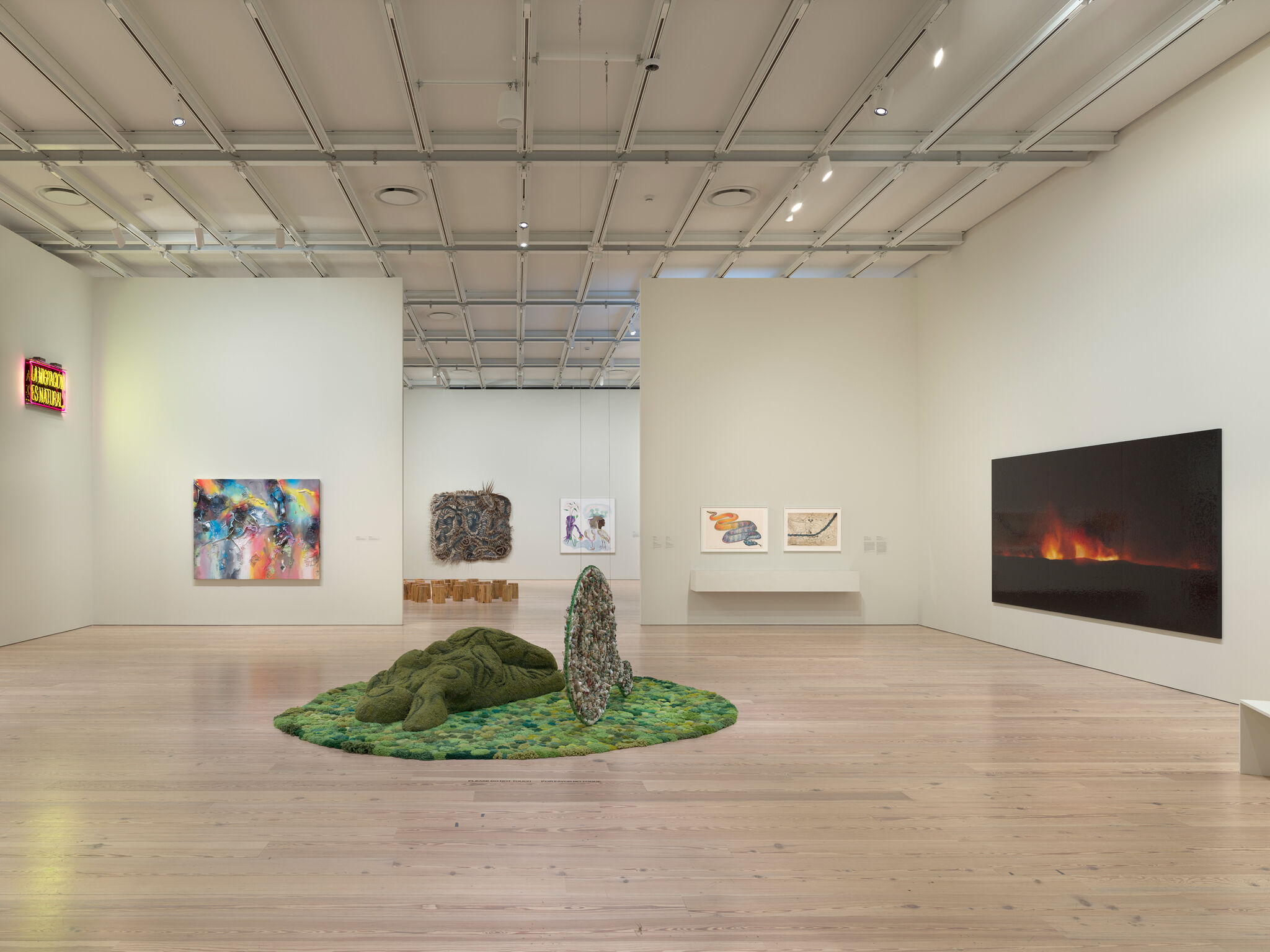 Art gallery with various paintings and sculptures, including a green textured installation on the floor and a large fiery landscape on the wall.