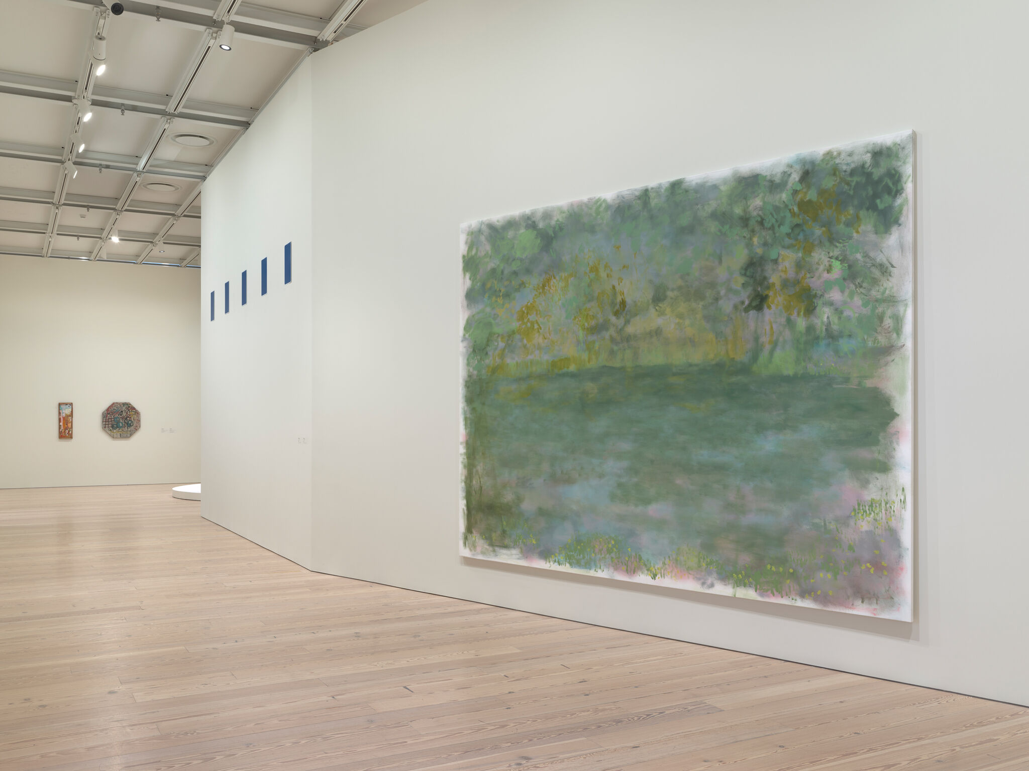 Art gallery with large abstract landscape painting on the right, smaller artworks on the left wall, and wooden flooring.