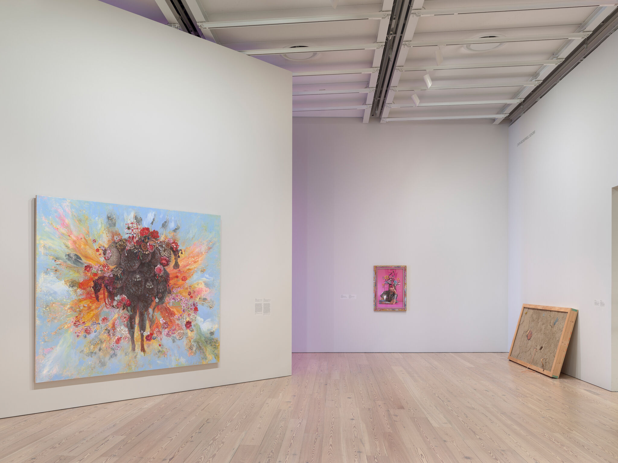 Art gallery with two colorful paintings on white walls, featuring vibrant abstract designs. One large piece on the left, a smaller one in the center.