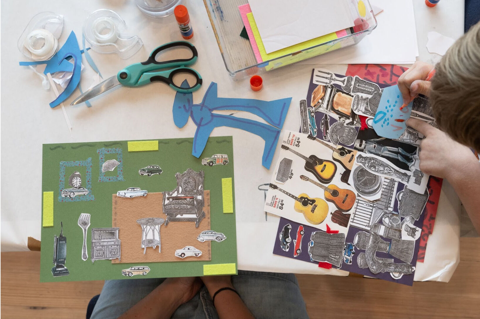 A photo showing a creative collage-making activity. A table is covered with art supplies, including scissors, tape, glue sticks, and cut-out shapes. Two hands are actively working on a collage, arranging colorful paper pieces, vintage cut-out images of cars, musical instruments, and furniture on a green background.