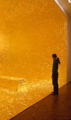 Person standing in front of a large, illuminated golden wall, creating a reflective and glowing atmosphere in a dimly lit room.