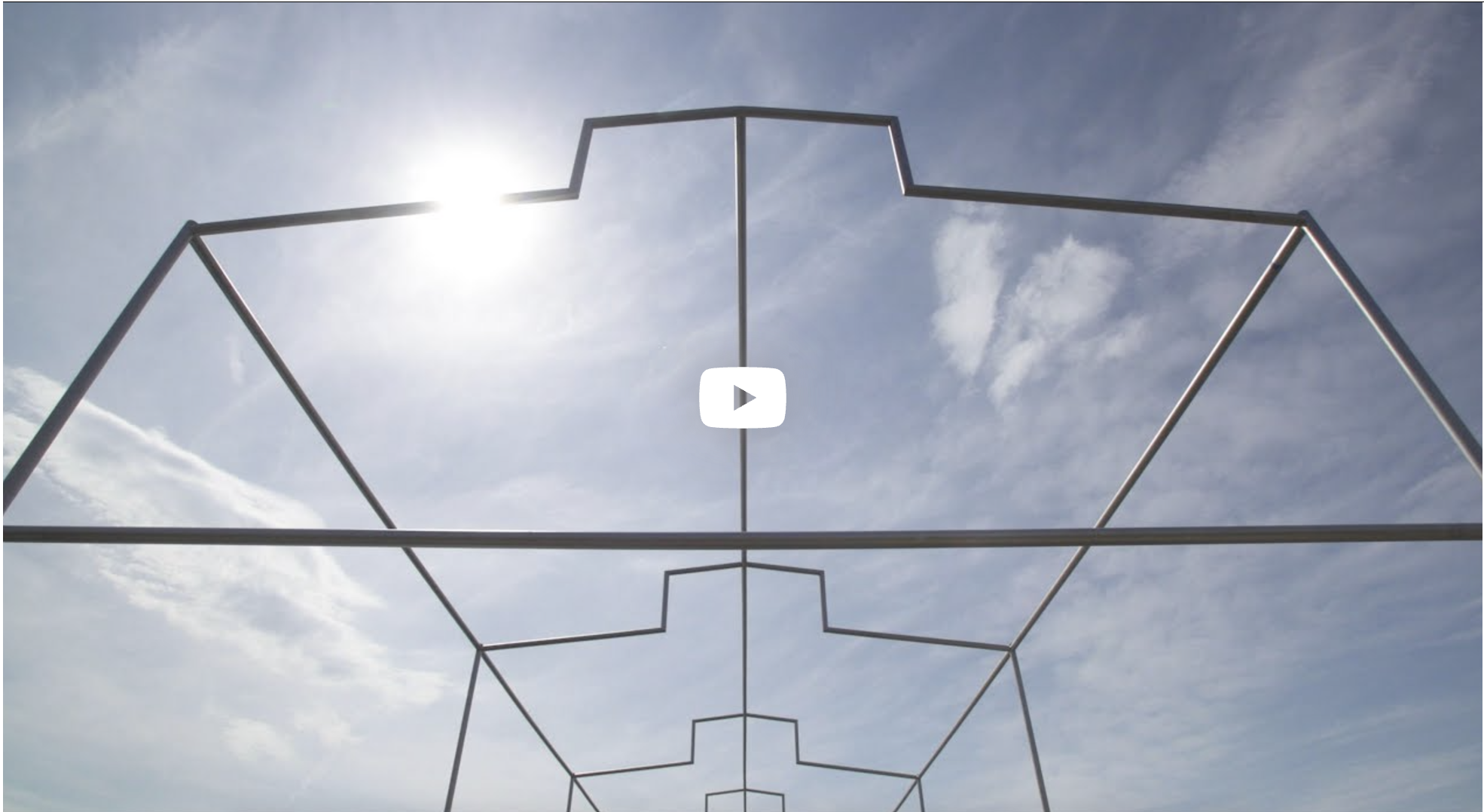 Metal framework against a blue sky with clouds, sun shining brightly.