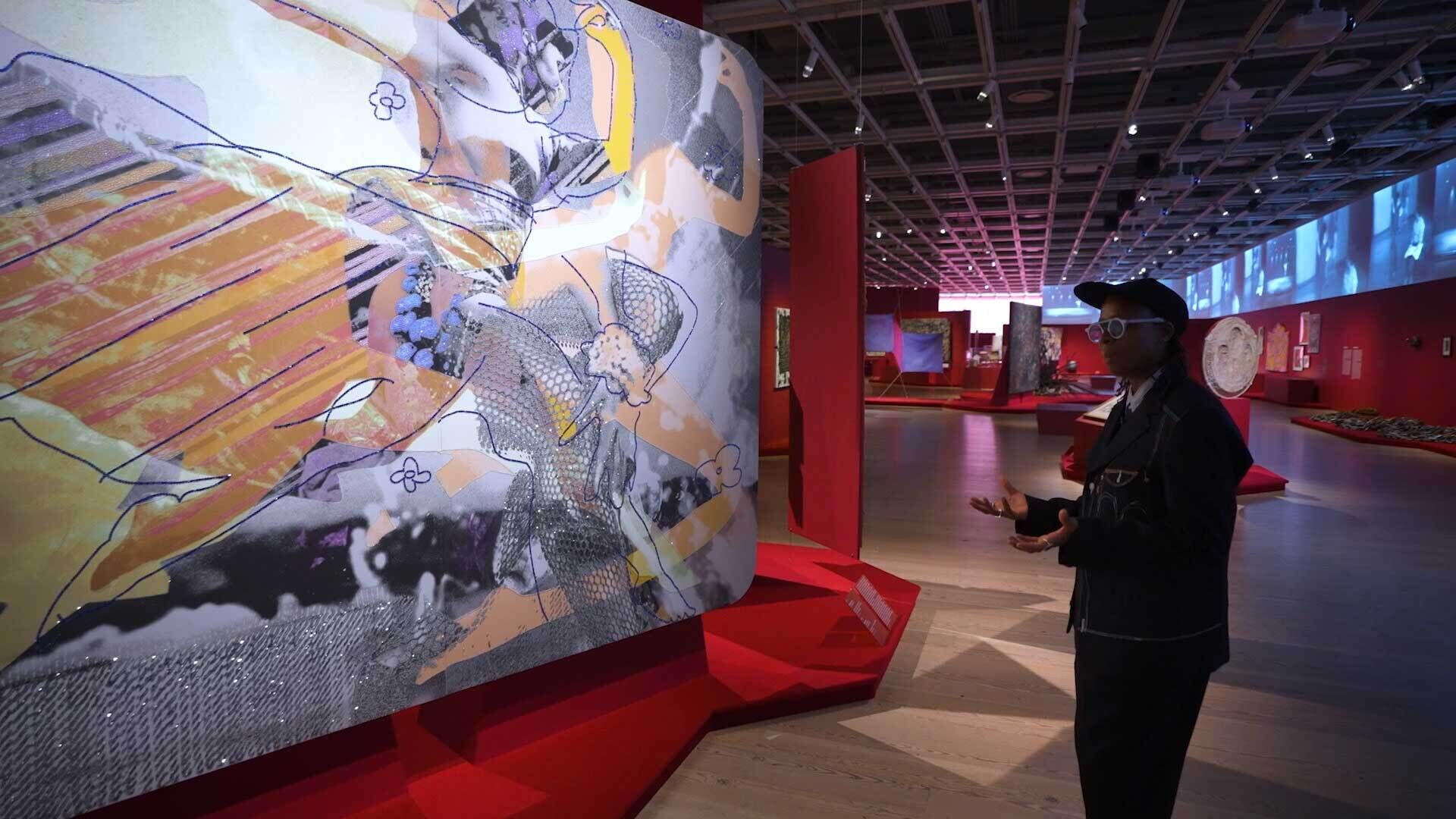 Person in a gallery viewing a large, colorful abstract artwork on a red display, with more art pieces visible in the background.