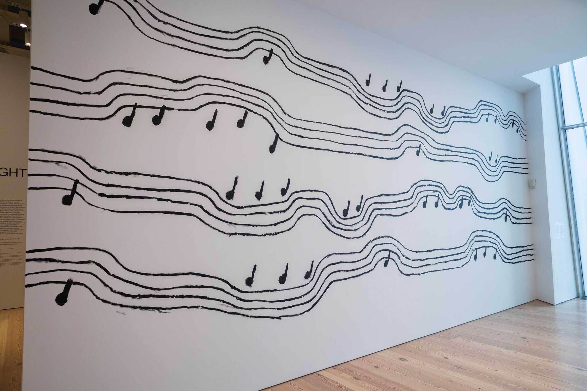 Black musical notes on wavy staff lines painted on a white wall in a gallery setting.