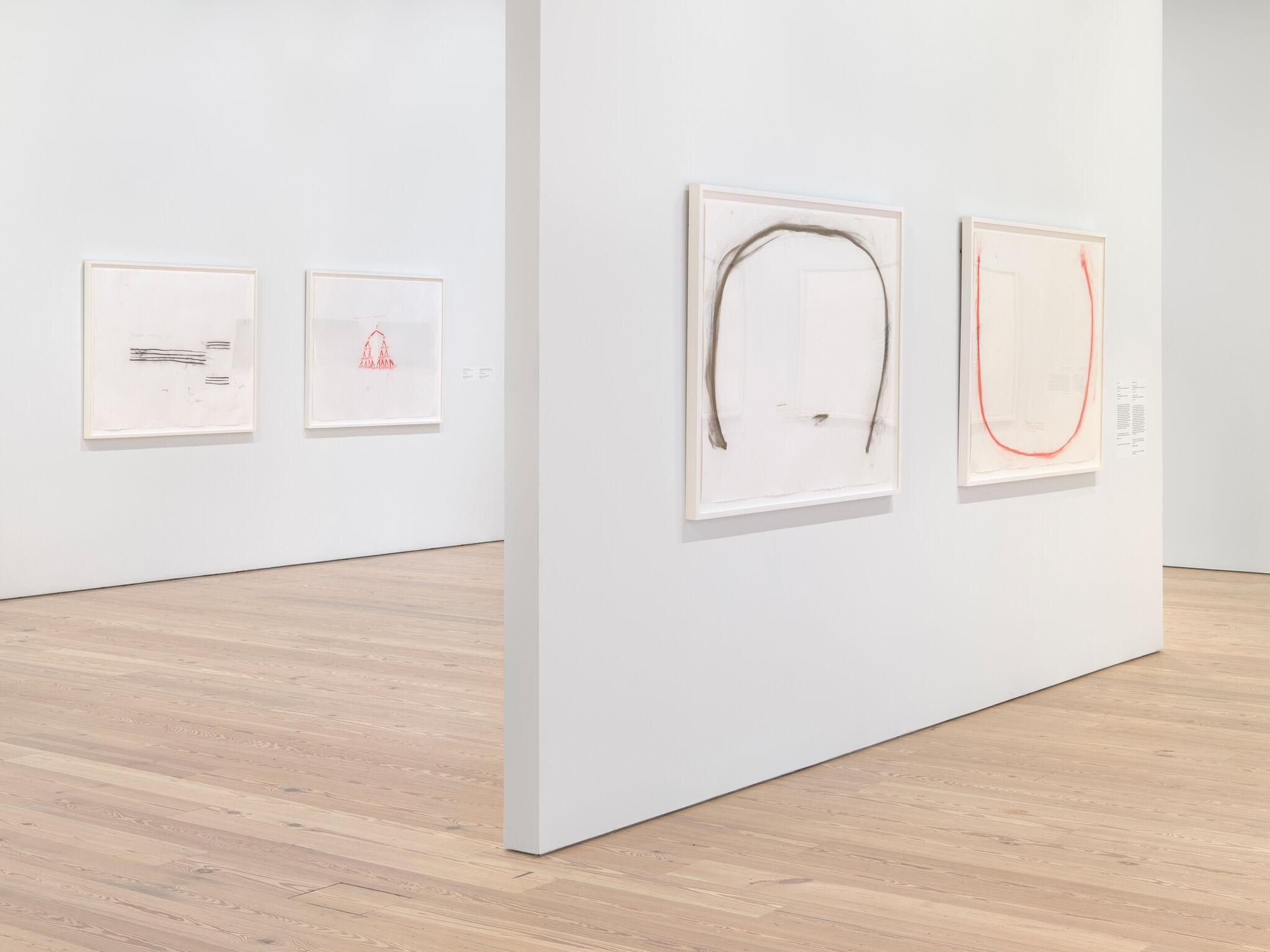 Art gallery with minimalist drawings on white walls, featuring abstract lines and shapes in black and red. Light wooden floor.