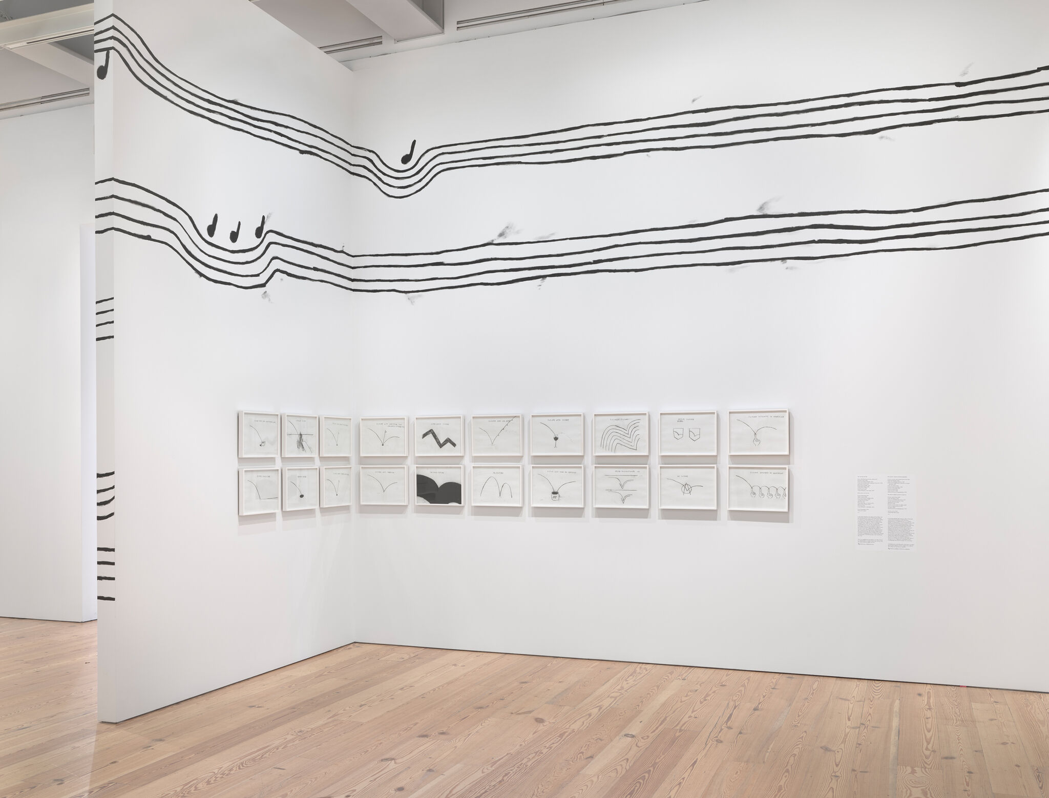 Art gallery with musical staff lines and notes painted on walls, featuring framed abstract drawings arranged in a grid on a wooden floor.