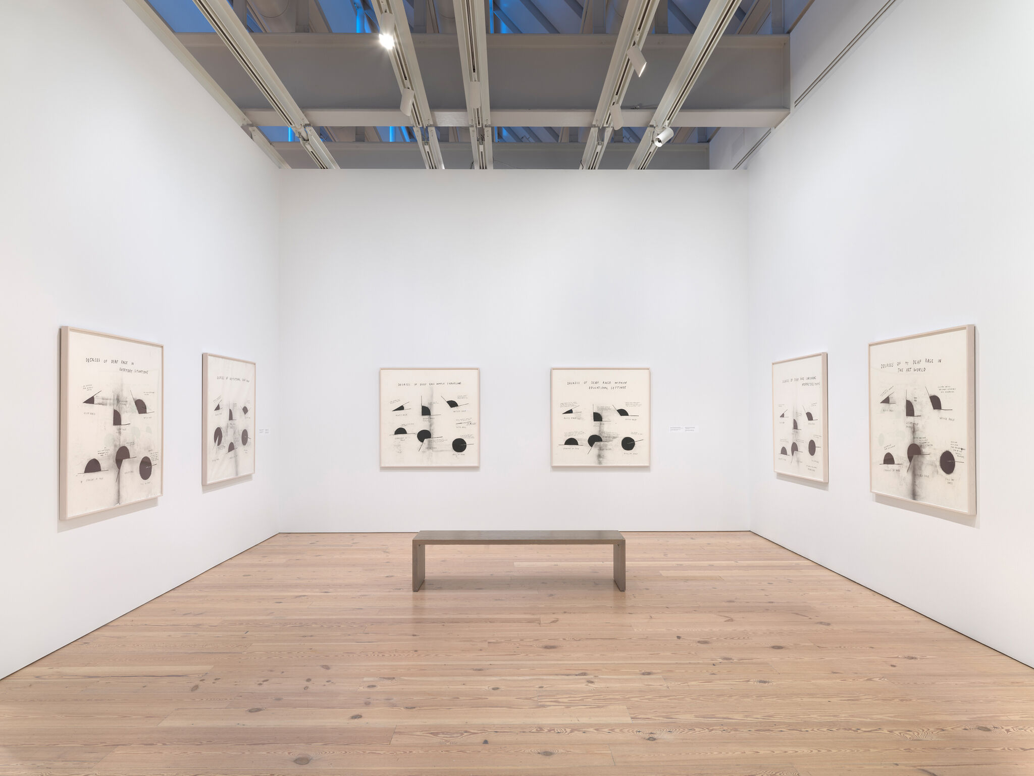 Art gallery room with six abstract black and white framed artworks on white walls, wooden floor, and a simple bench in the center.