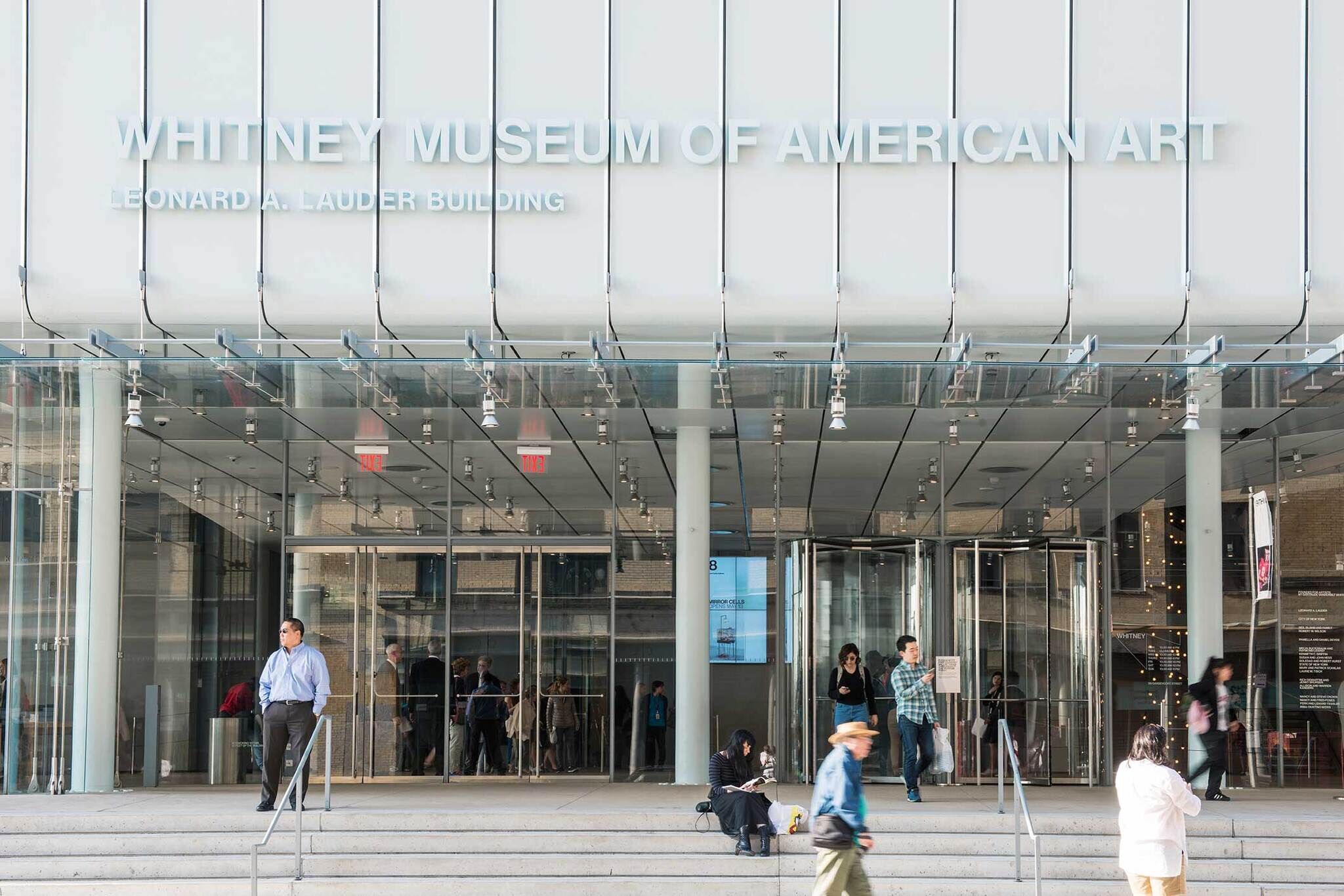 Entrance of the Whitney Museum of American Art, Leonard A. Lauder Building, with people walking and sitting outside.