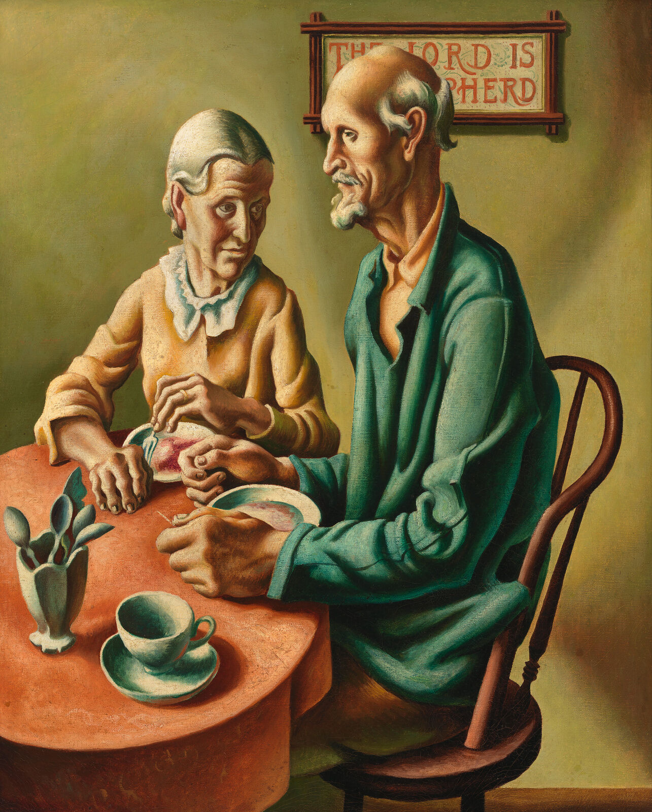 An older couple sits at a modest table with a small plate in front of each and other empty dishes nearby. Visible behind them but half hidden by the man’s head, a country style plaque reads “the lord is my shepherd.”