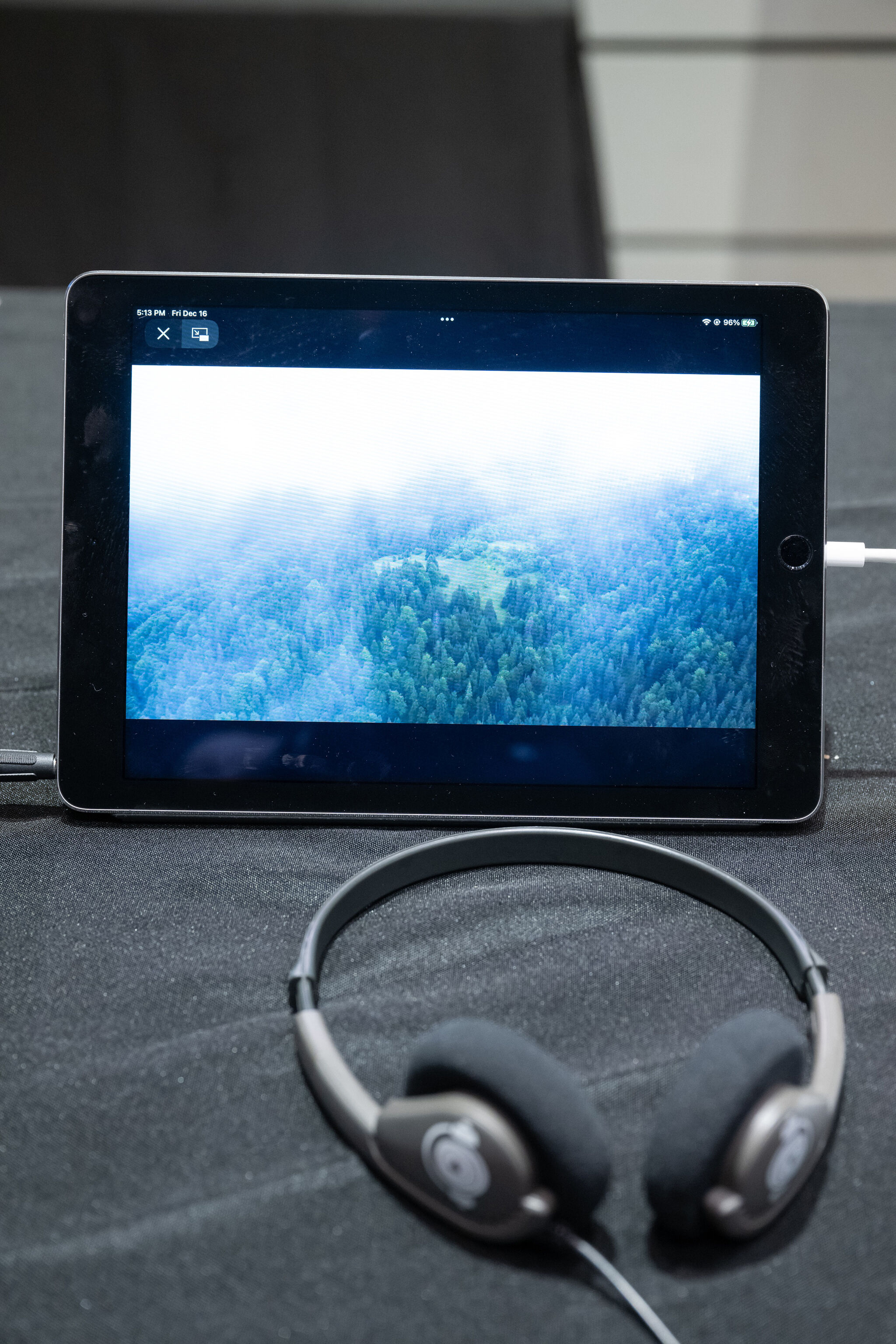 Tablet displaying a misty forest scene, placed on a black surface with headphones in front.