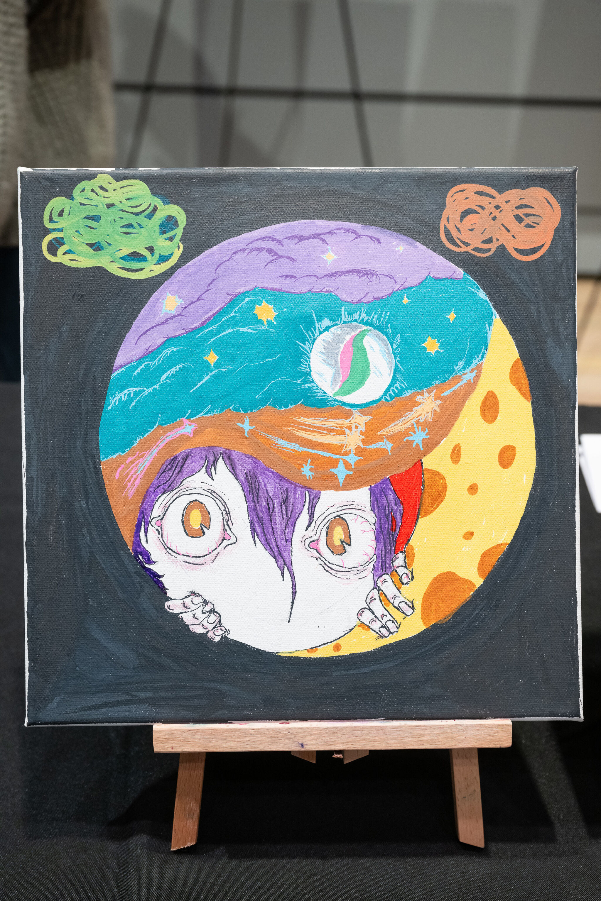 Colorful painting of a wide-eyed character with purple hair, surrounded by cosmic elements and abstract shapes on a canvas.