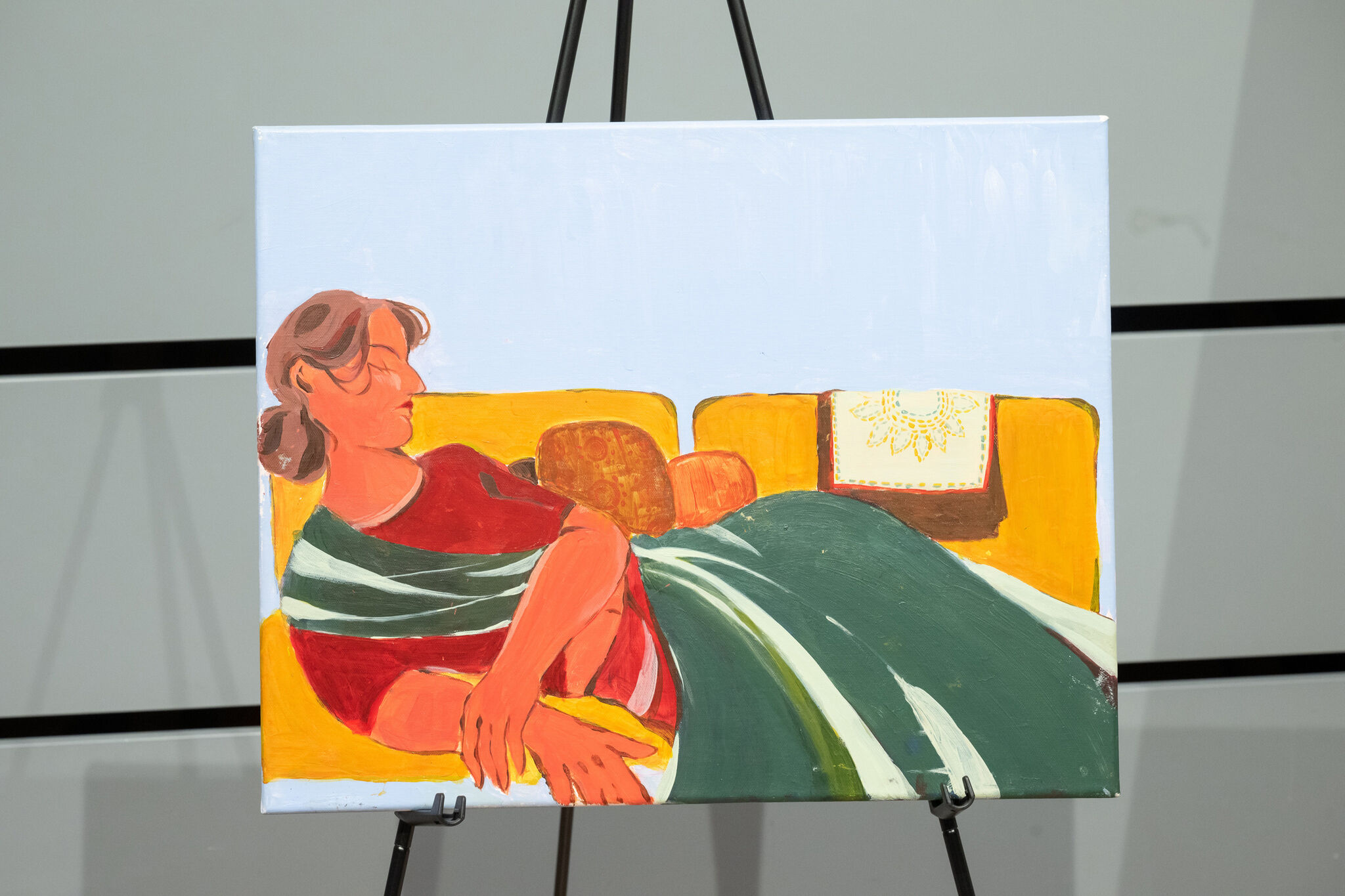 Painting of a person reclining on a yellow couch, wearing a red top and green blanket, with a decorative pillow in the background.