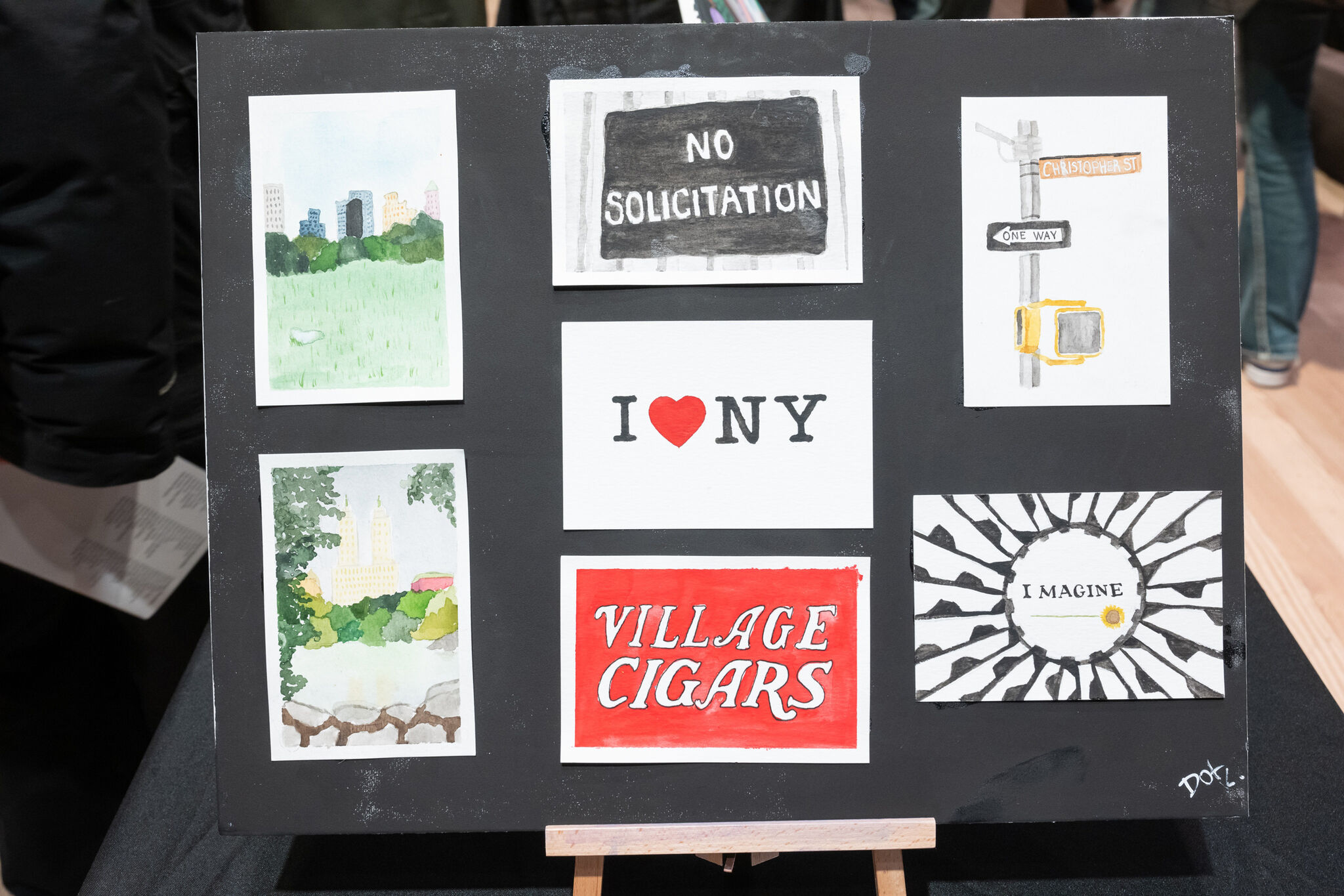 A display board with six artworks, including "I ❤️ NY," "Village Cigars," and "No Solicitation" signs, plus cityscapes and street signs.