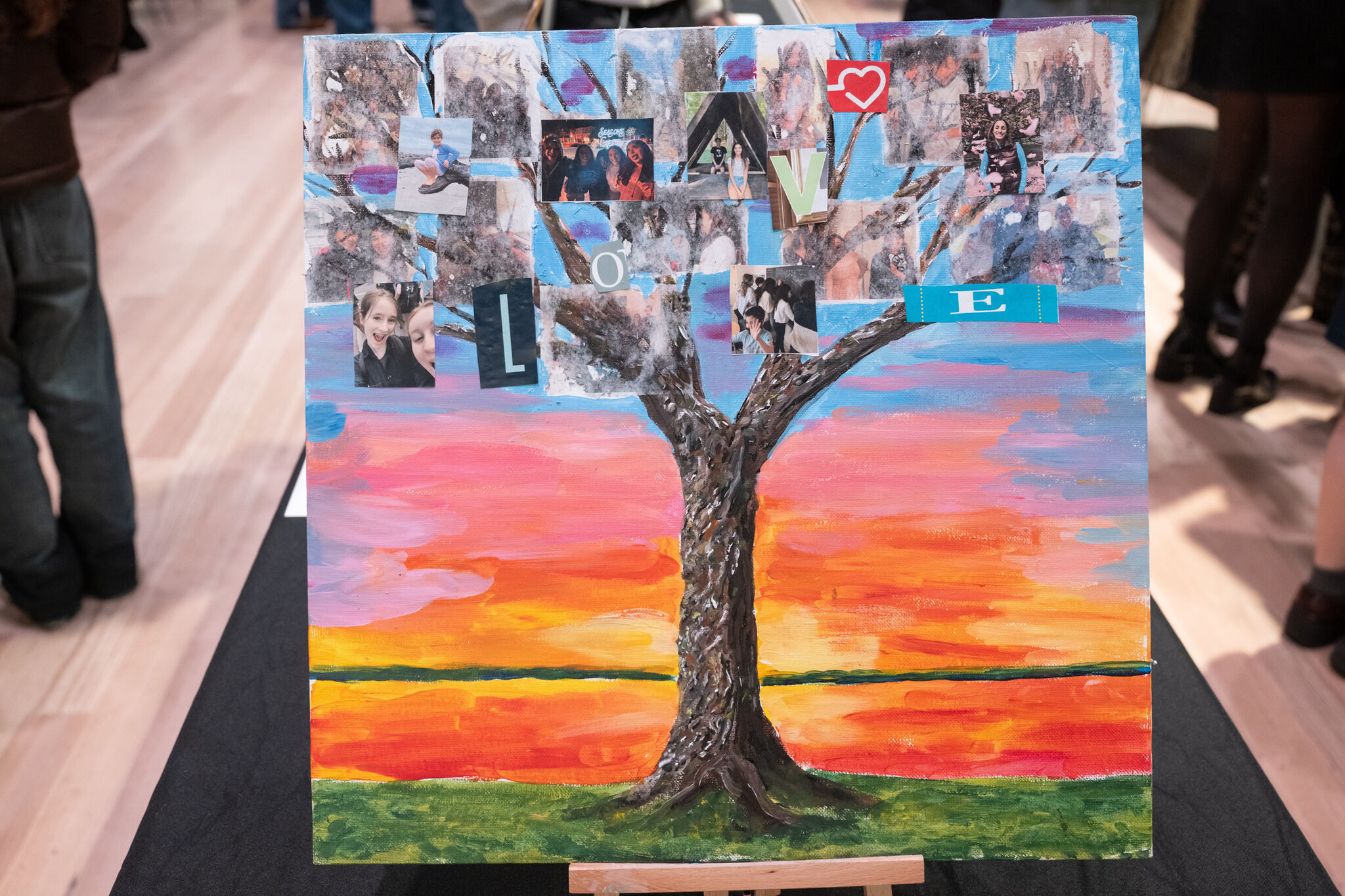 Colorful painting of a tree with photo collage leaves and the word "LOVE" on branches, set against a vibrant sunset background.