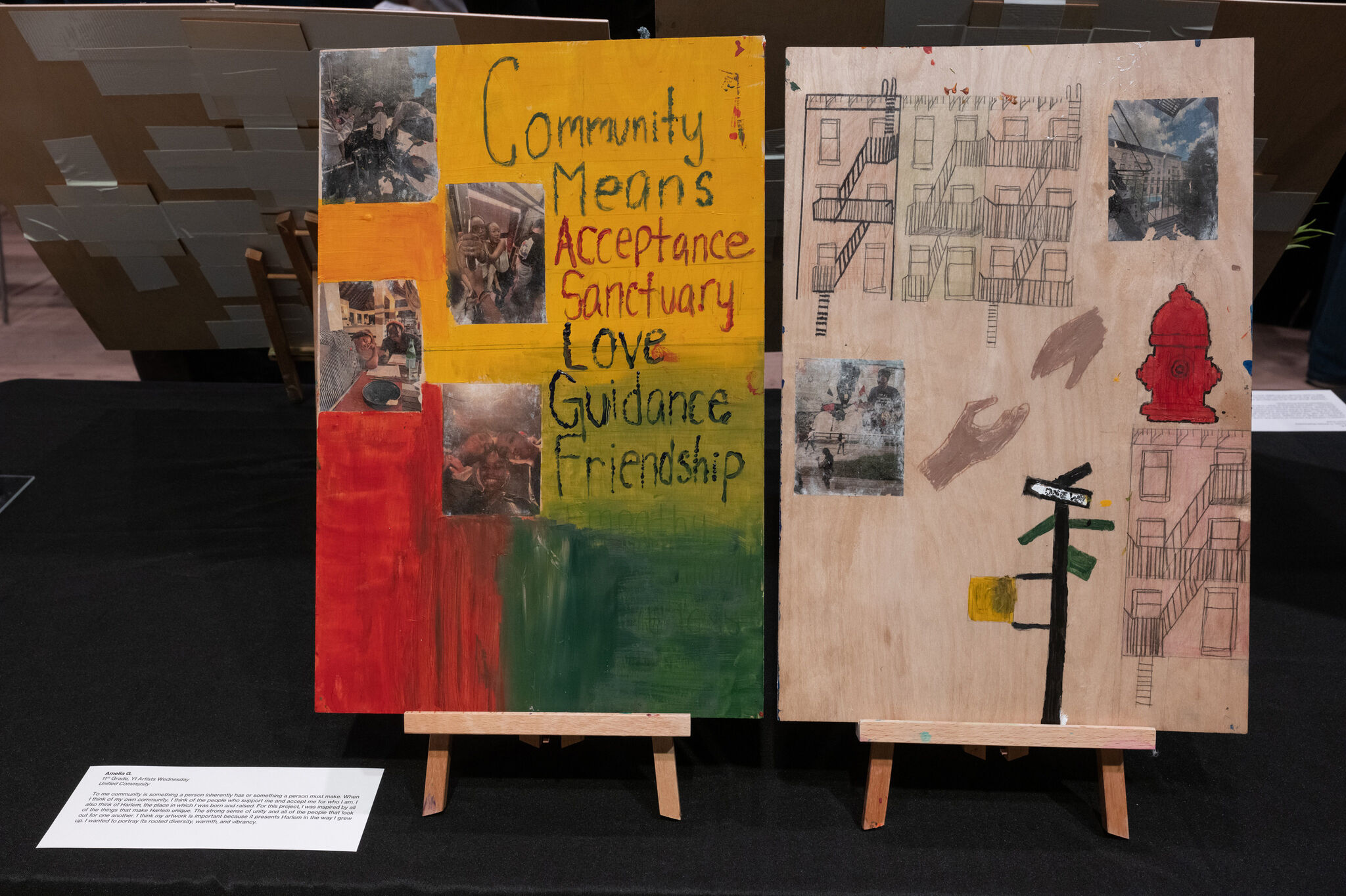 Two art pieces on easels. Left: colorful with words "Community Means Acceptance Sanctuary Love Guidance Friendship" and photos. Right: sketches of buildings.