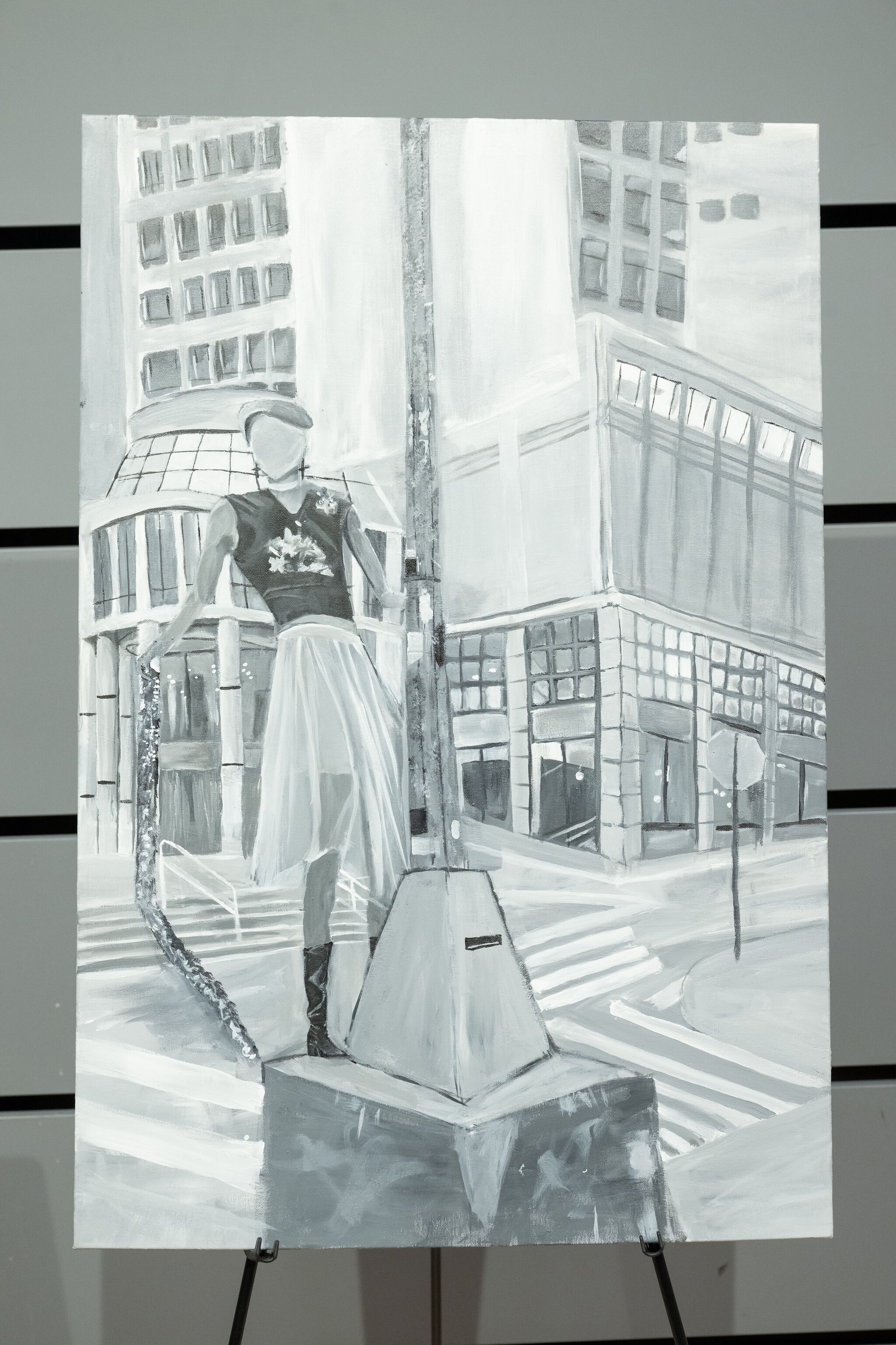 Black and white painting of a faceless figure in a skirt and top, standing on a city street corner with tall buildings in the background.