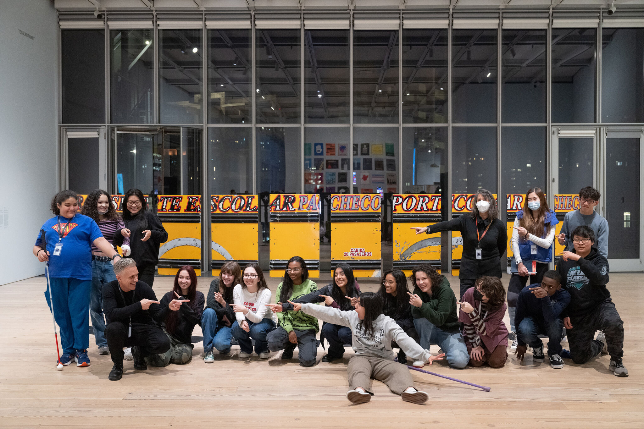 A group of people posing and pointing at each other in front of a yellow and black art installation inside a gallery.