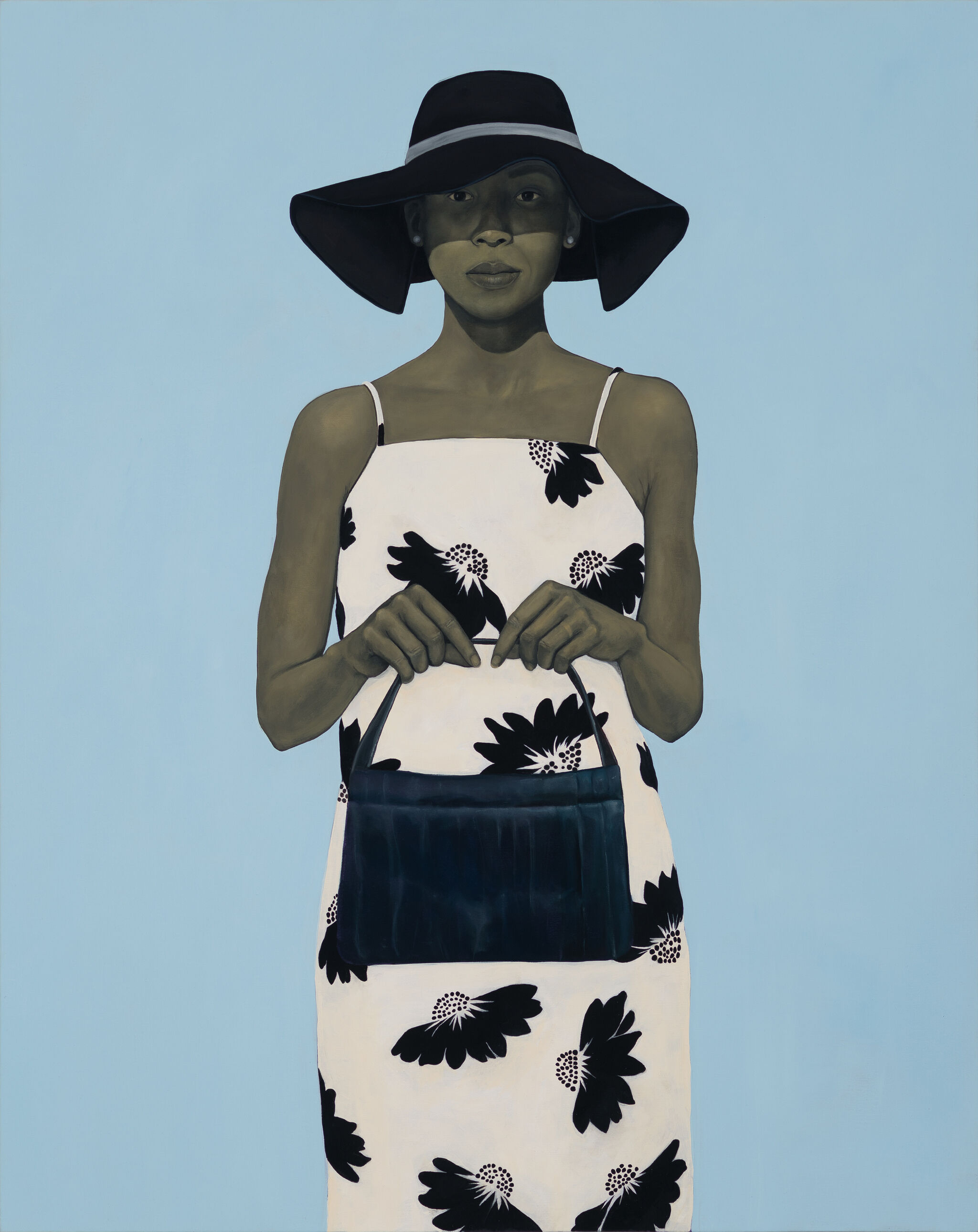 Woman in a floral dress and wide-brimmed hat holds a black handbag against a light blue background.